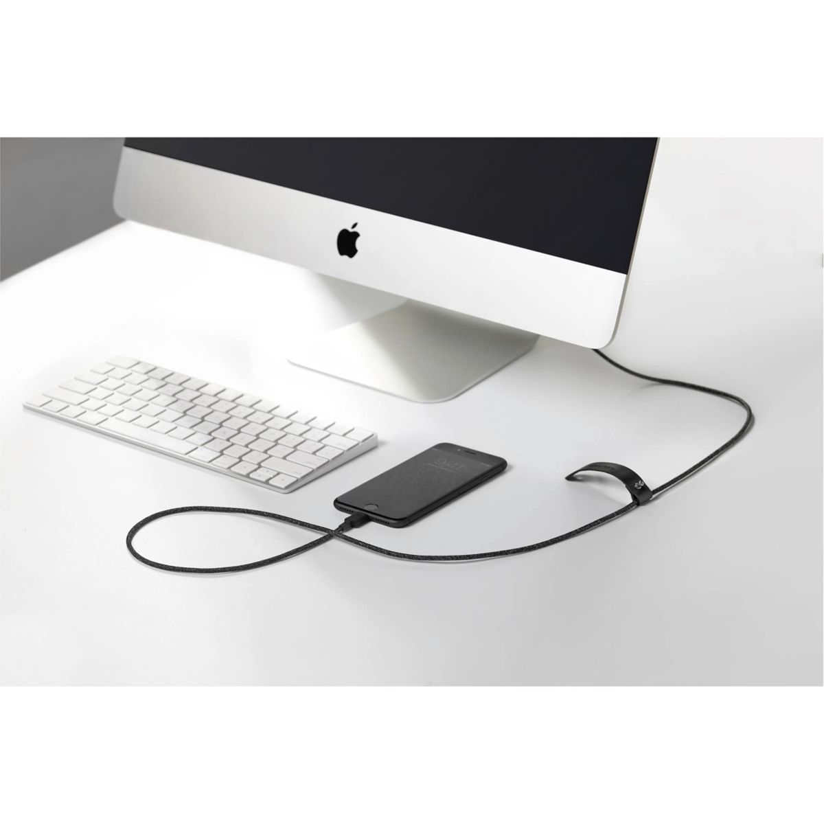 Un iMac, tastiera e iPhone su una scrivania bianca, collegati da un cavo.