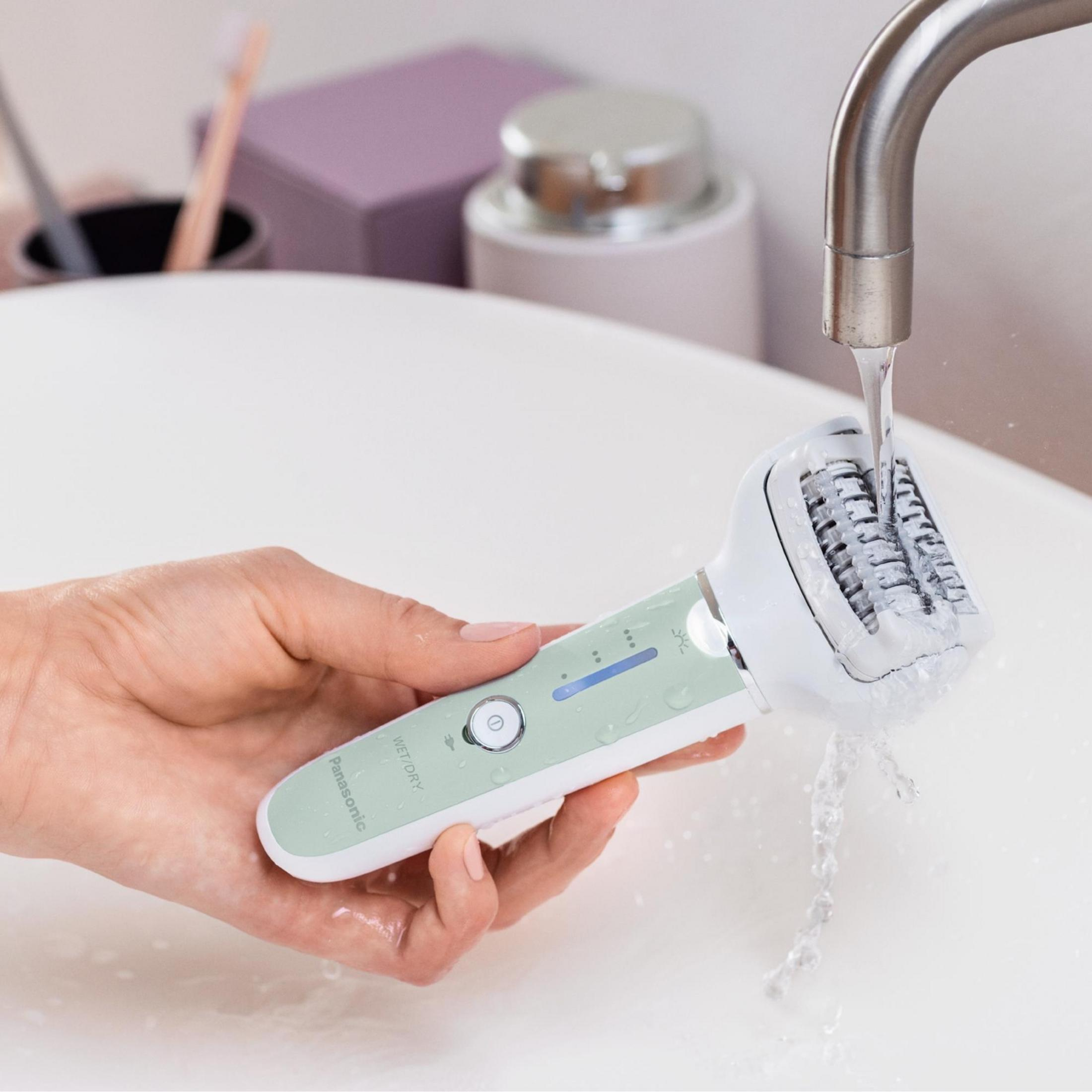 Eine Hand hält einen Panasonic Epilierer unter fließendem Wasser in einem Waschbecken.