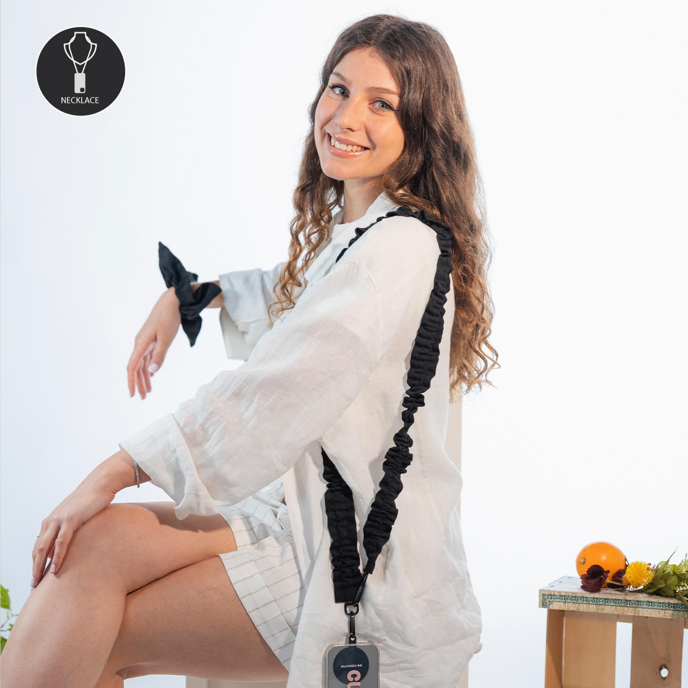 Una mujer joven con pelo rizado sonríe, viste camisa blanca y collar.