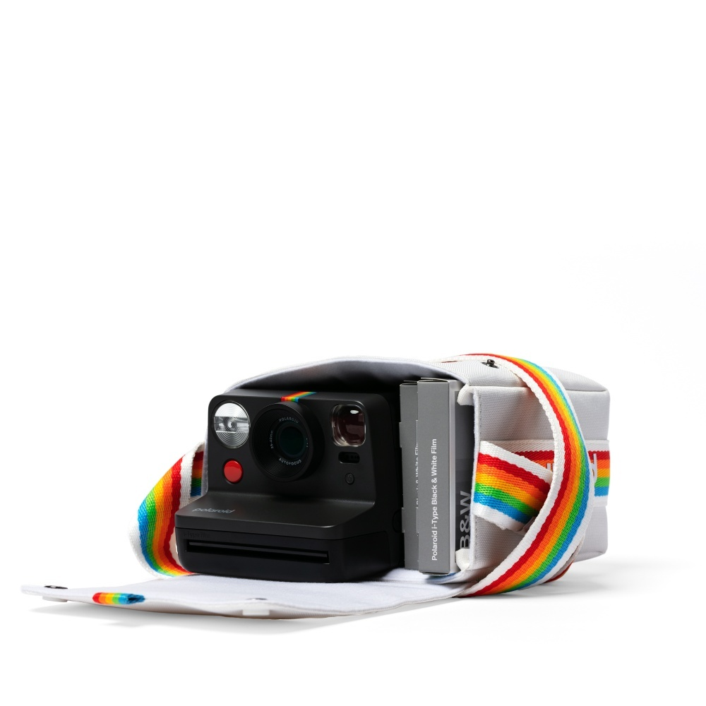 Eine schwarze Polaroid-Kamera mit Regenbogenband und Filmpack in einer weißen Hülle.
