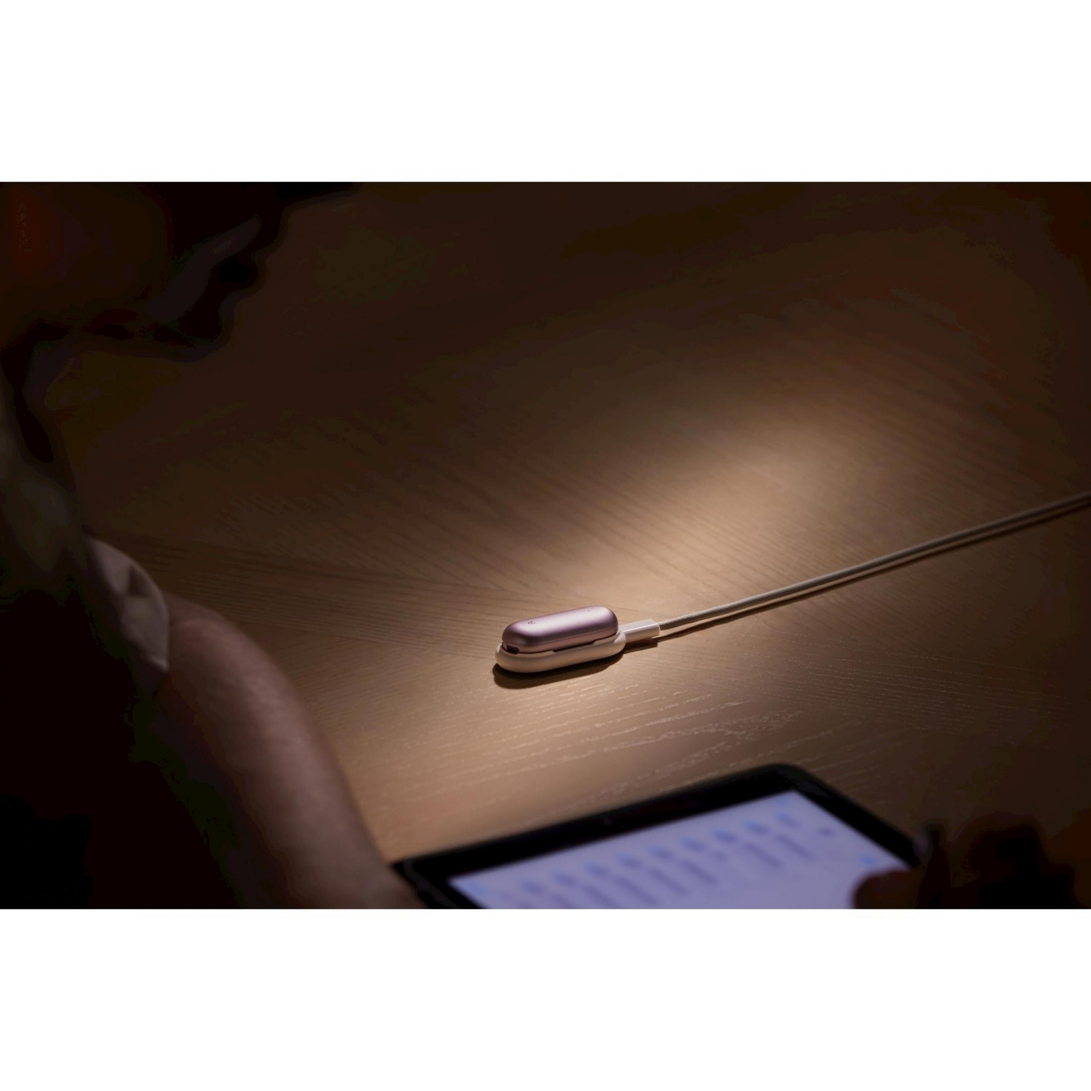 Un estuche de carga rosa dorado con cable blanco descansa sobre mesa madera.