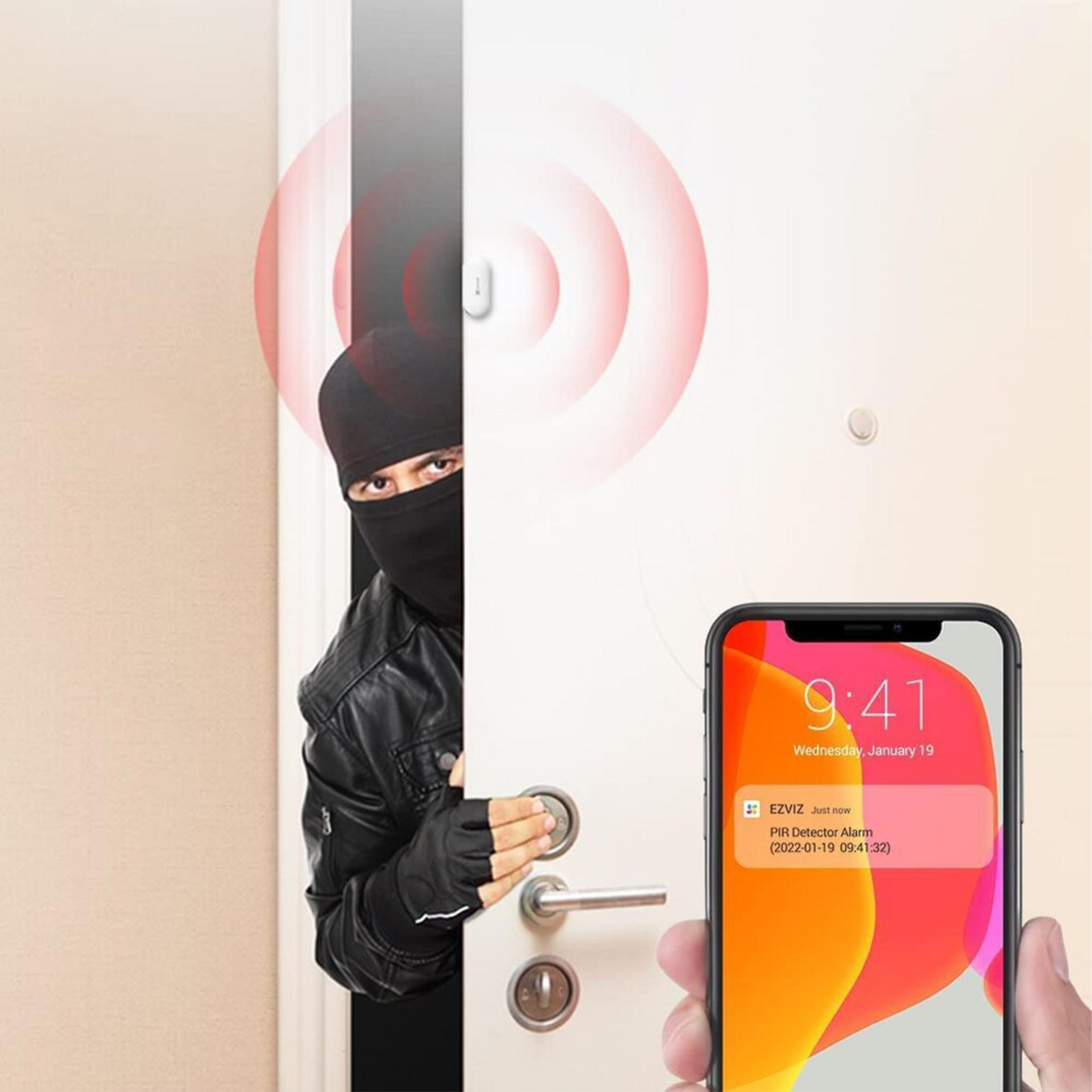 Un ladrón con pasamontañas abre una puerta. Un teléfono muestra una alerta.