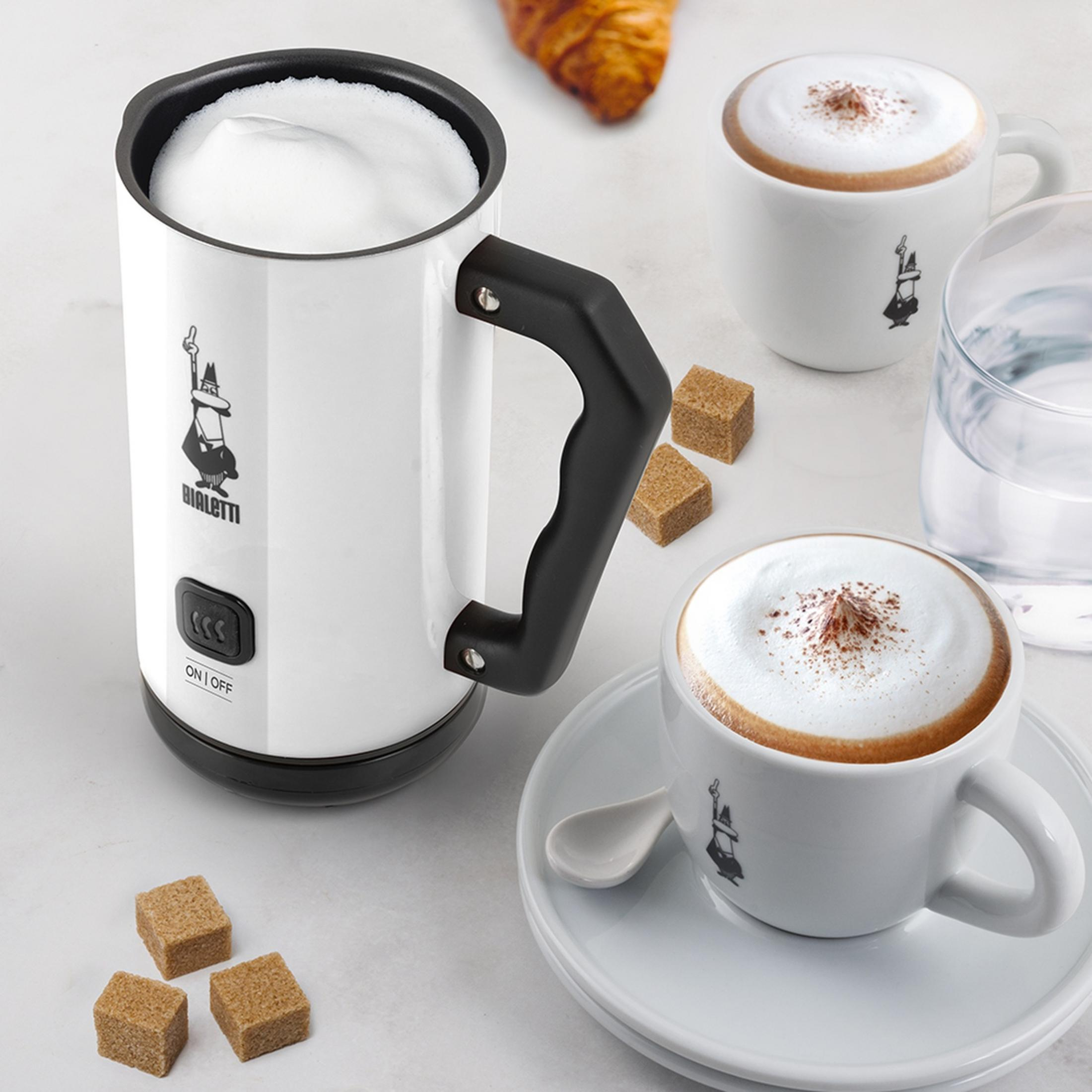 Un montalatte bianco con schiuma, due tazzine da caffè, zollette di zucchero e un bicchiere d'acqua.