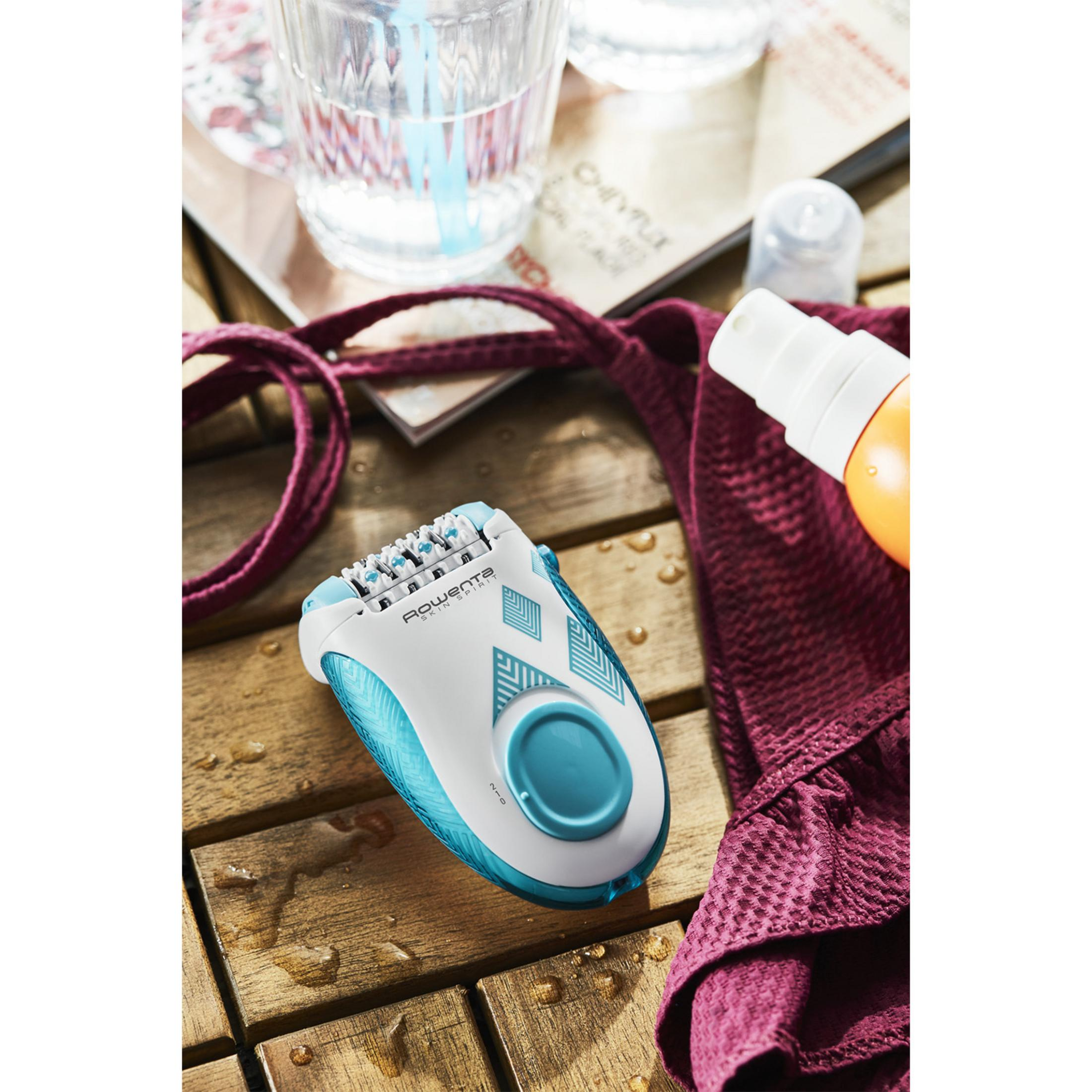 Depilator na drewnianym stole z plamami wody, obok ręcznika i kremu z filtrem przeciwsłonecznym.