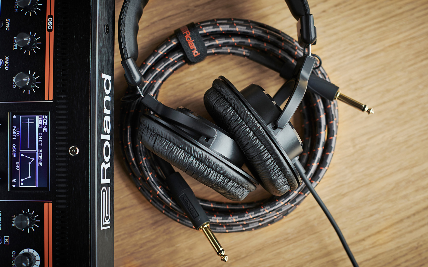 Schwarze Kopfhörer mit Kabel liegen auf einem Holzschreibtisch neben einem schwarzen Roland Synthesizer.