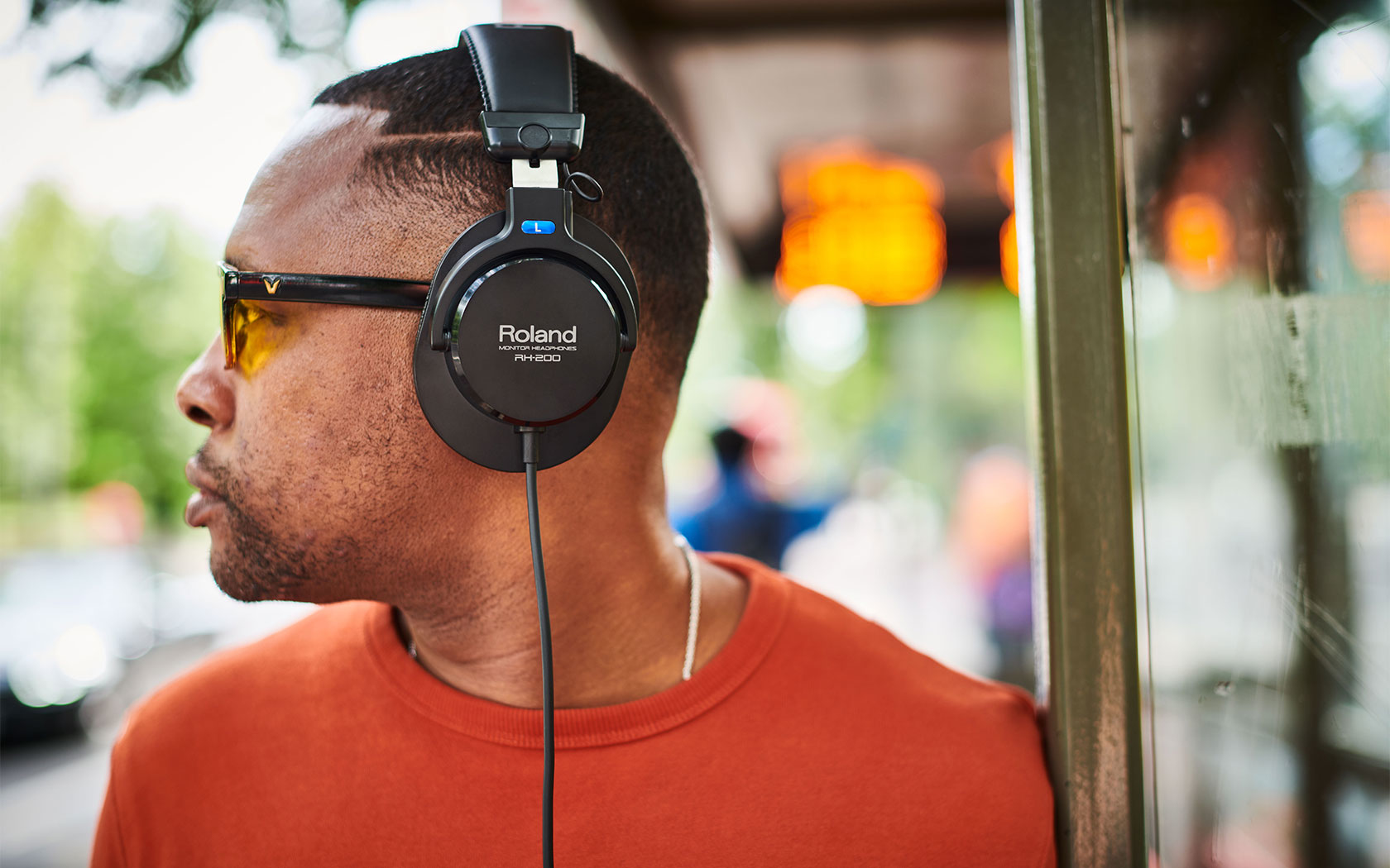 Mann mit Kopfhörern und Sonnenbrille, der auf einen Bus wartet.