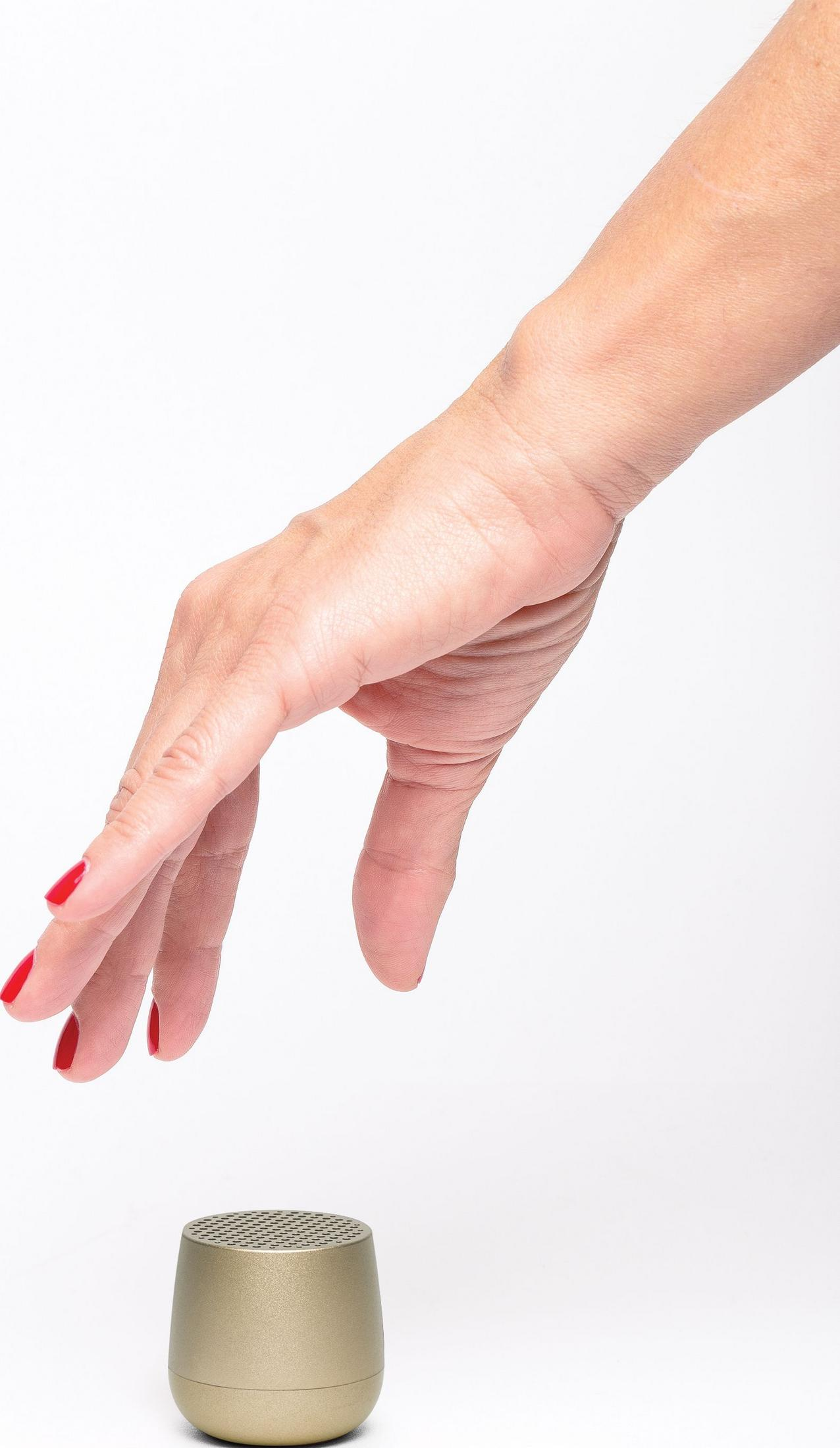 Una mano con unghie rosse si protende verso un piccolo altoparlante dorato.