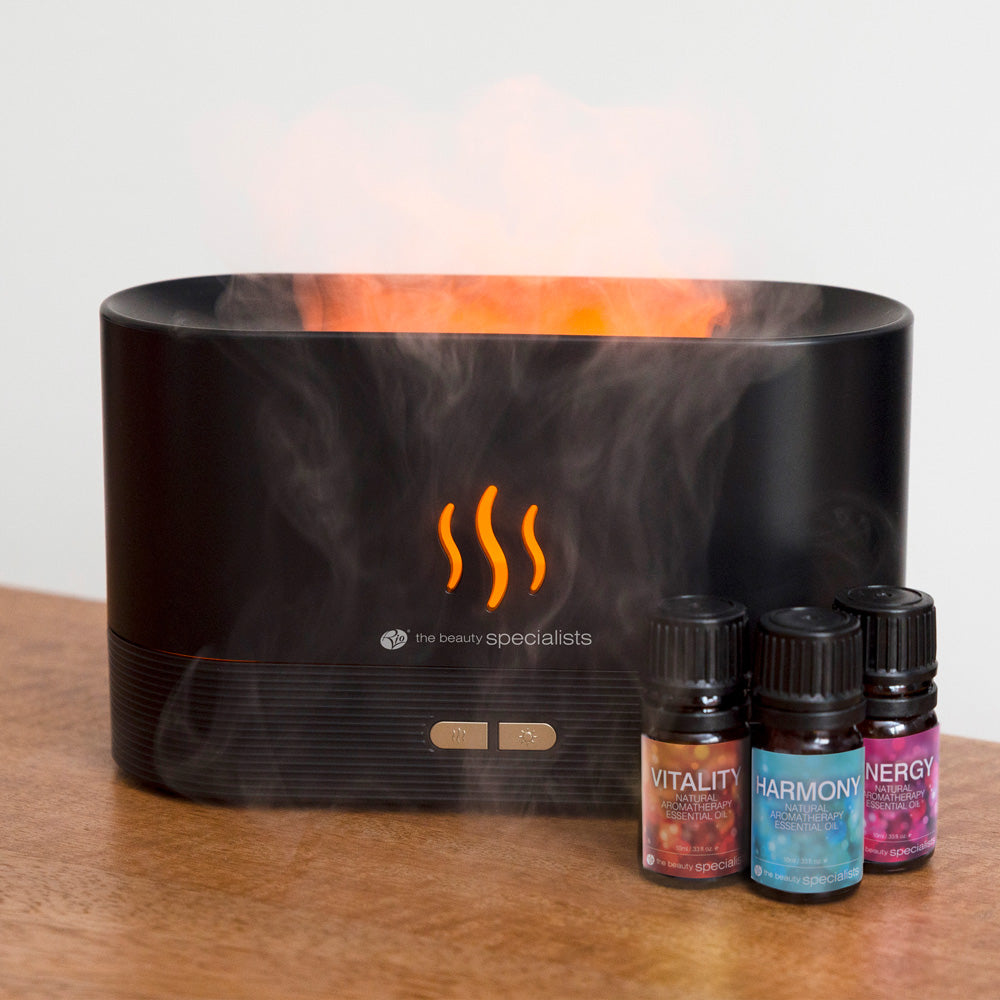 Ein schwarzer Aroma-Diffusor mit orangefarbenem Licht und Dampf steht neben drei ätherischen Ölflaschen.
