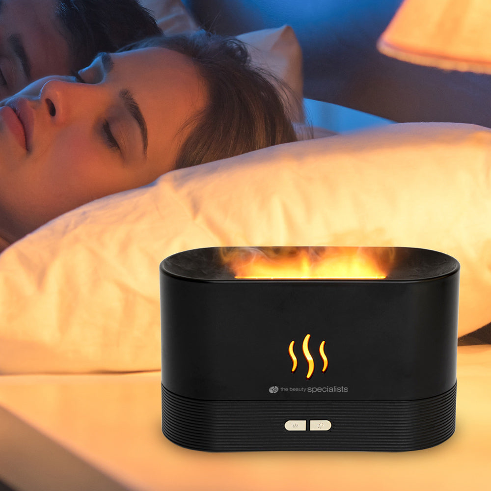 Ein schwarzer Diffusor mit Flammen-Effekt neben einem schlafenden Paar im Bett.