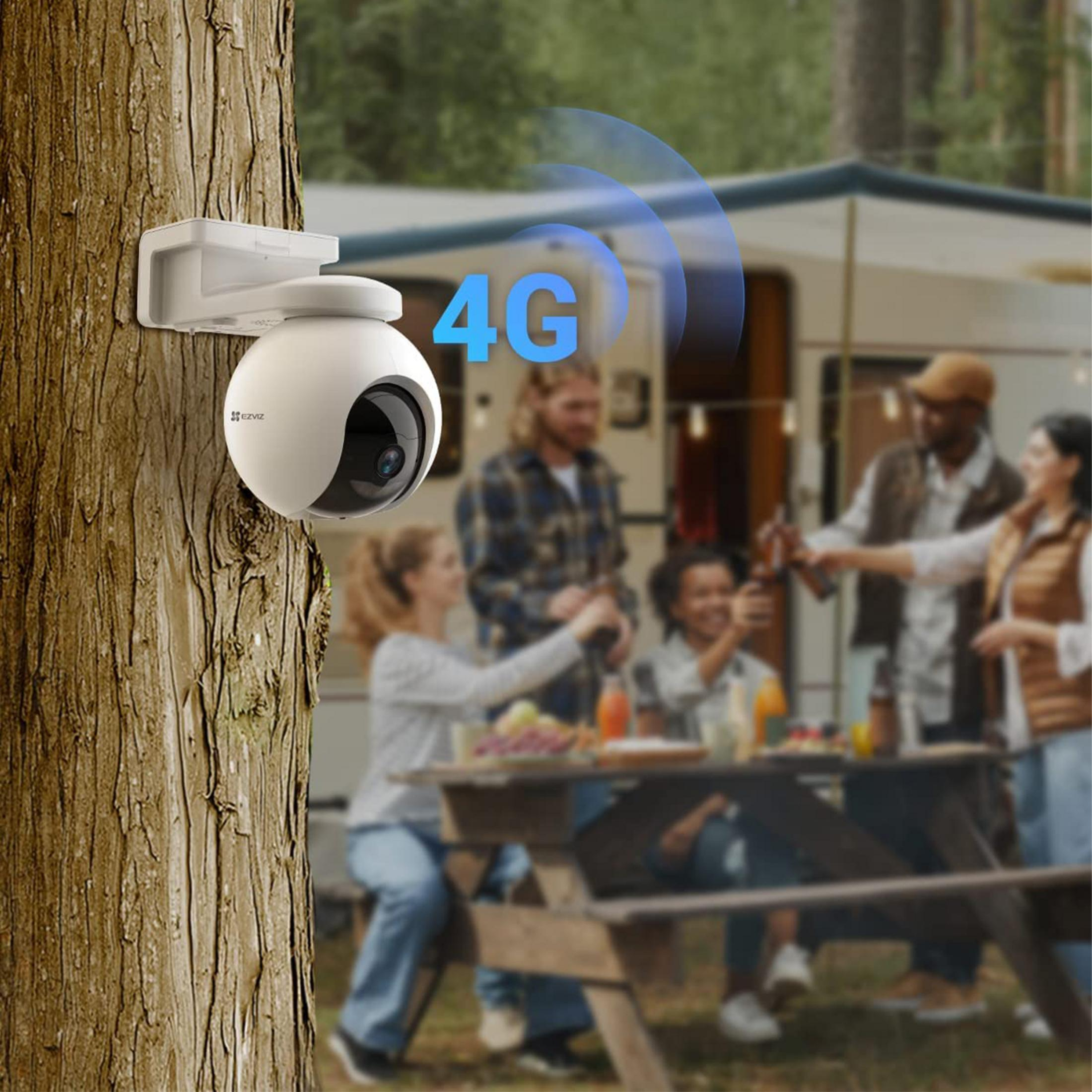 Biała kamera bezpieczeństwa na pniu drzewa, z piknikującymi ludźmi.