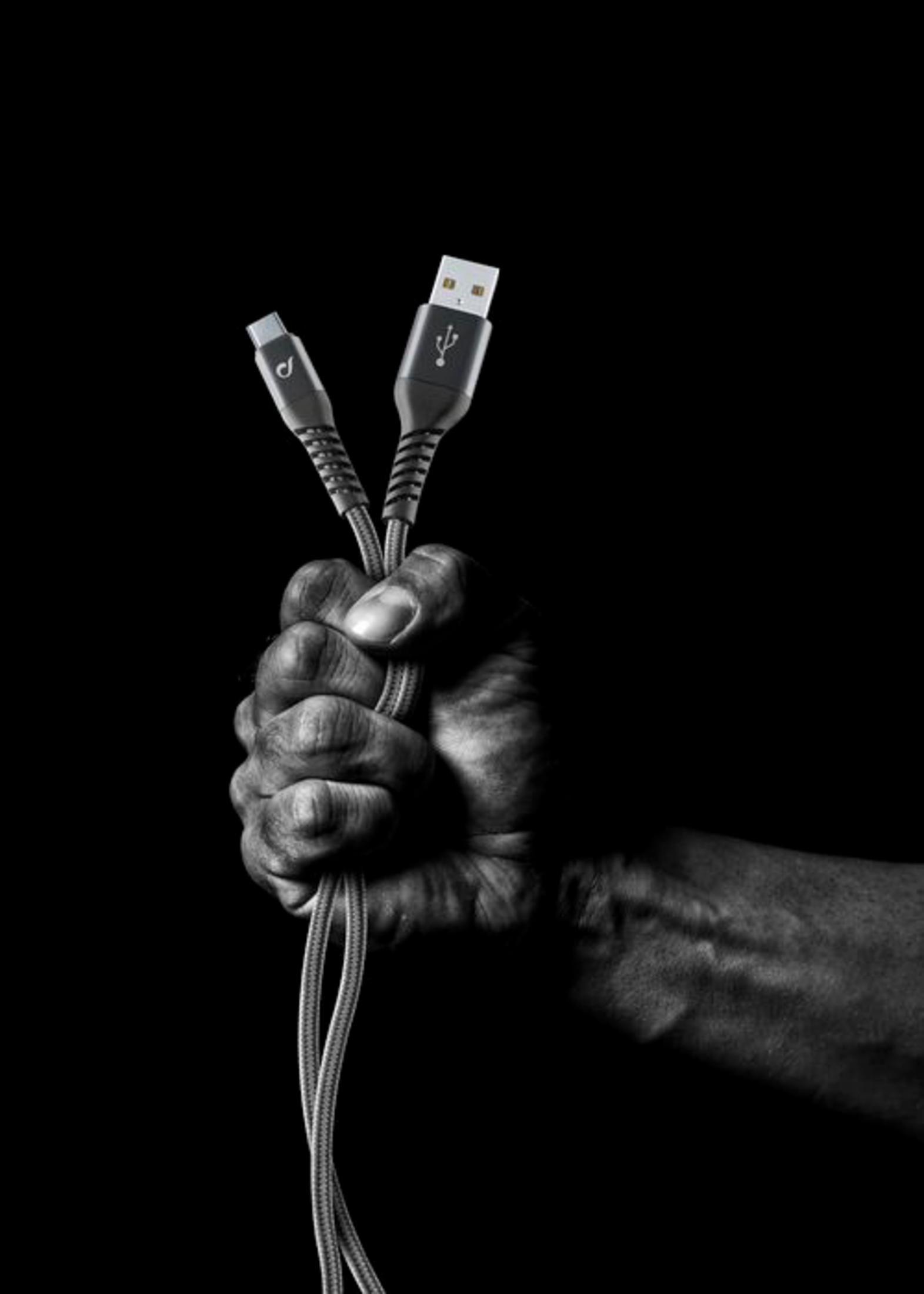 Una mano agarra dos cables USB con conectores negros sobre fondo negro.
