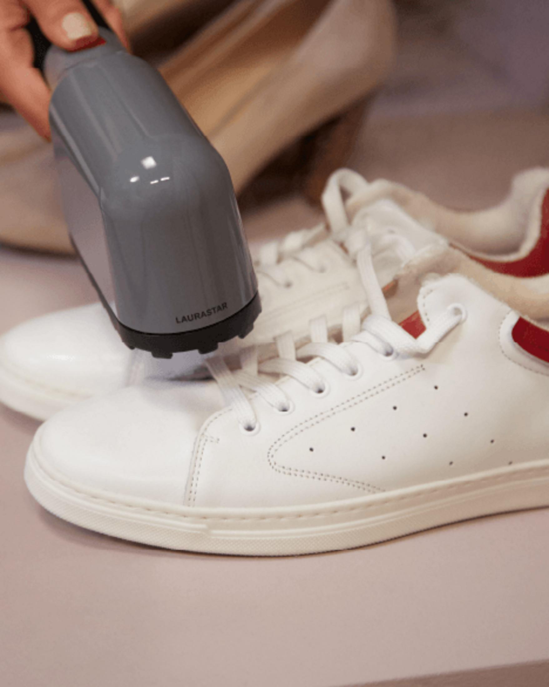 Ein graues Dampfgerät reinigt weiße Sneaker mit roten Akzenten.