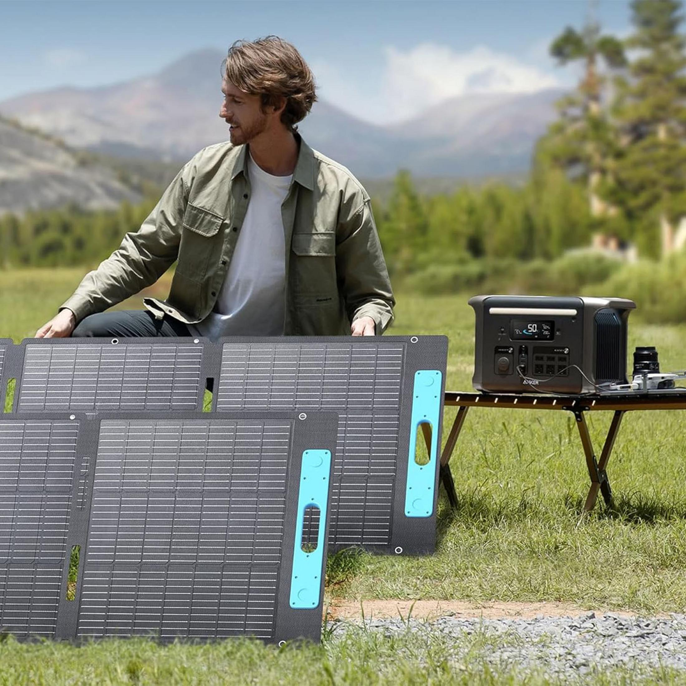 Mężczyzna siedzi przy panelach słonecznych i power station w górskim krajobrazie.