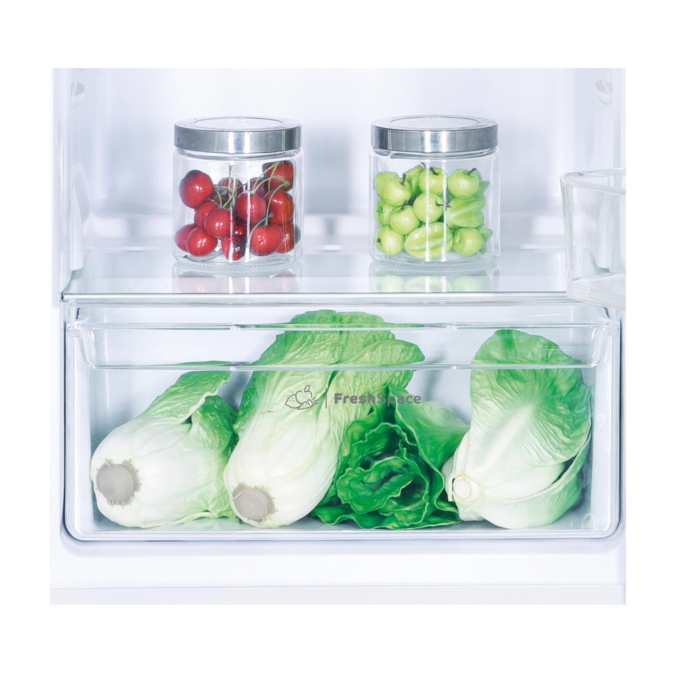 Dwa słoiki z wiśniami i zielonymi owocami nad sałatą w szufladzie lodówki.