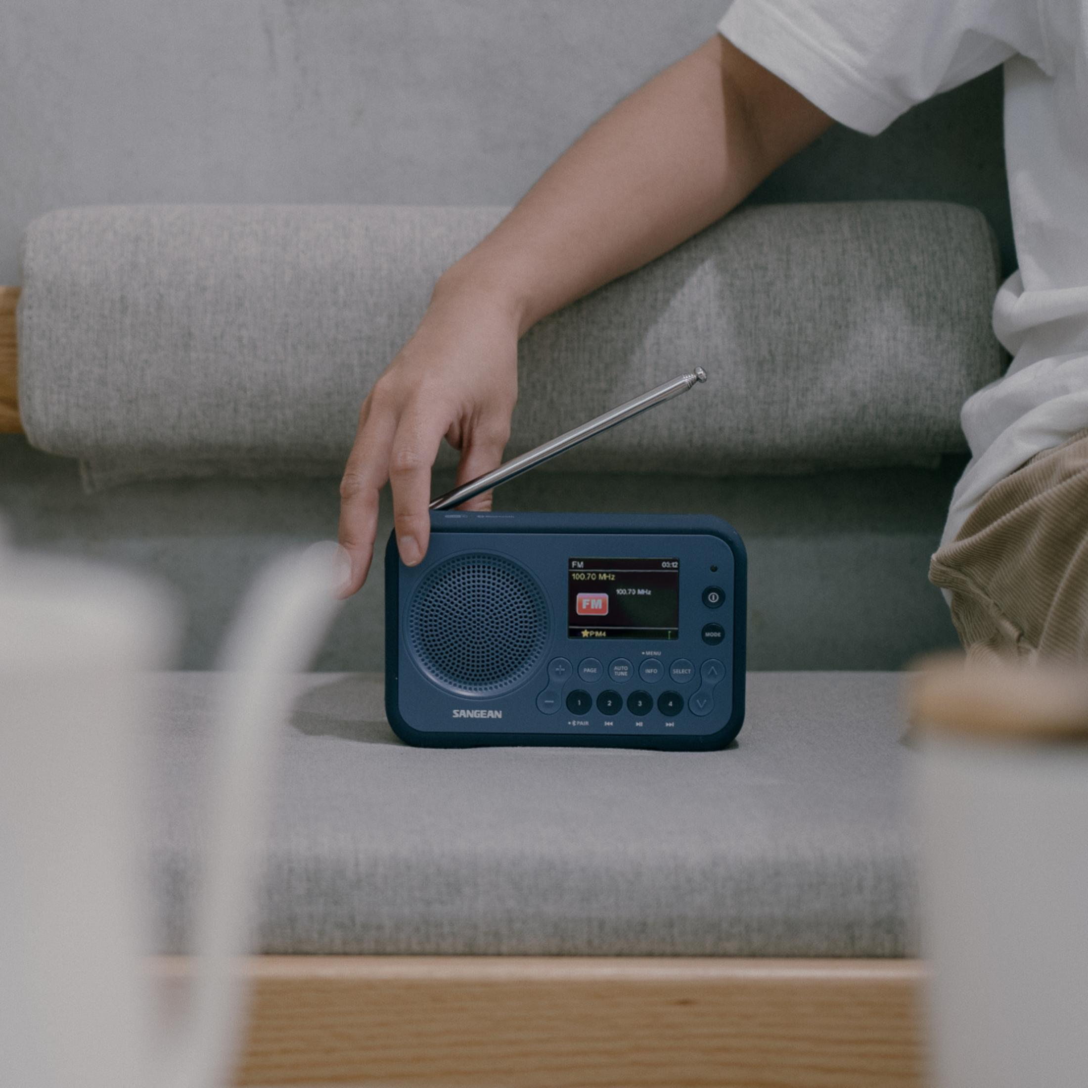 Une personne utilise une radio bleue sur un canapé. L'antenne est déployée.