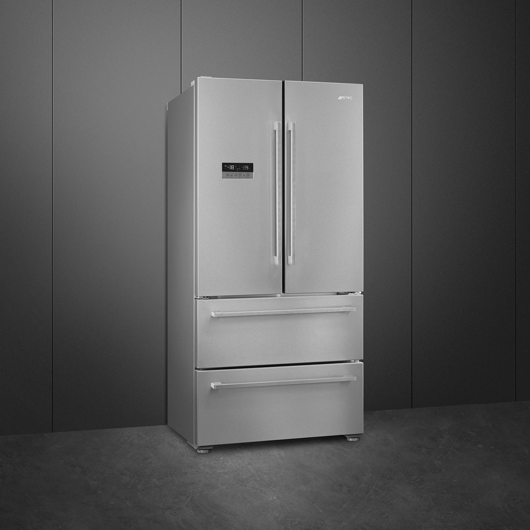 Un refrigerador plateado de tres puertas y cajones se alza ante una pared oscura.
