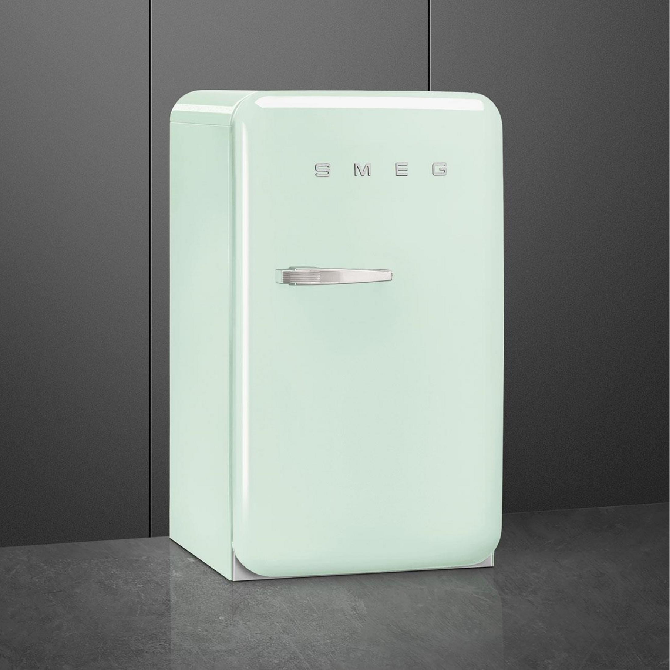 Un refrigerador SMEG verde pastel con asa plateada sobre suelo oscuro.