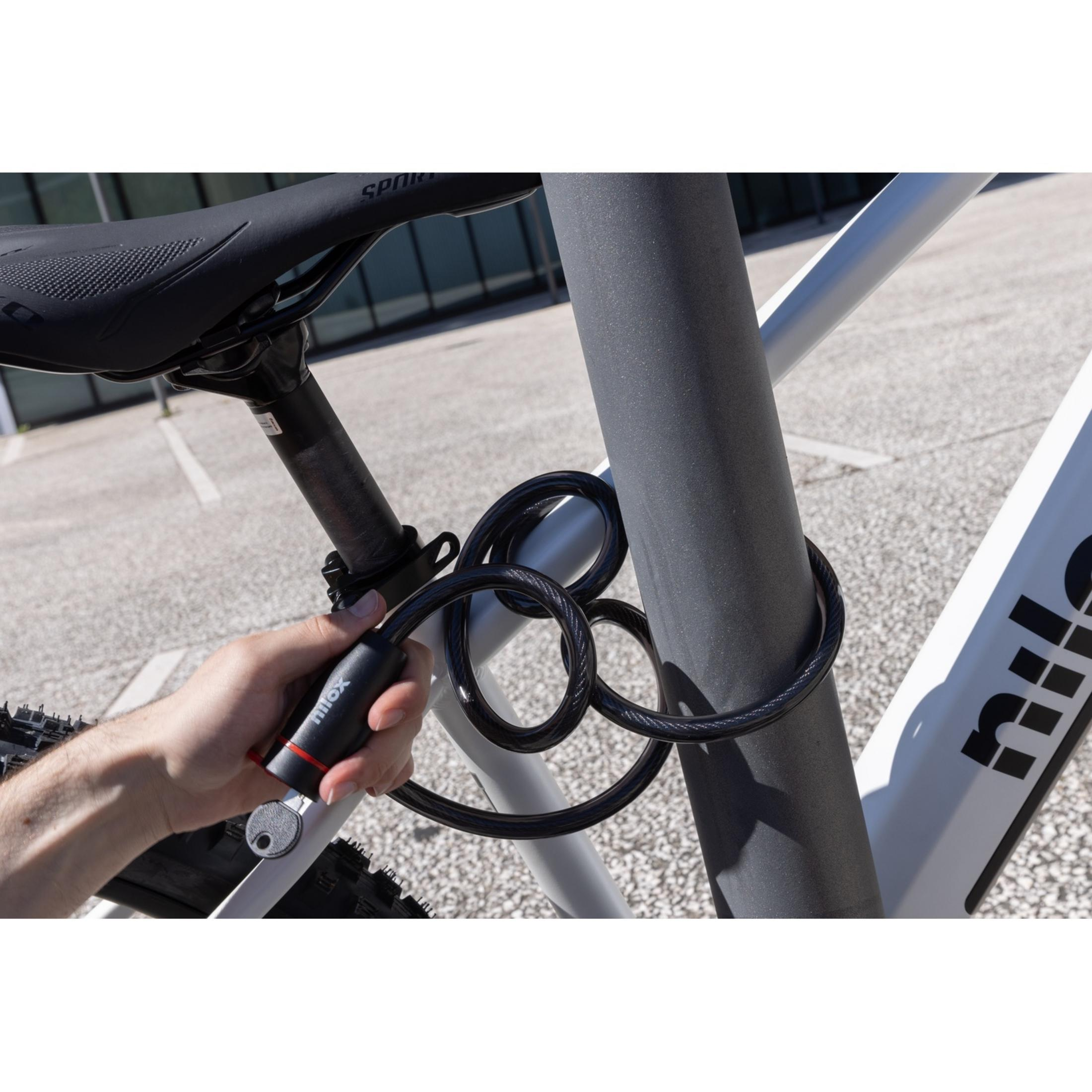 Eine Hand schließt ein schwarzes Fahrradschloss um eine Stange. Ein Fahrrad ist sichtbar.
