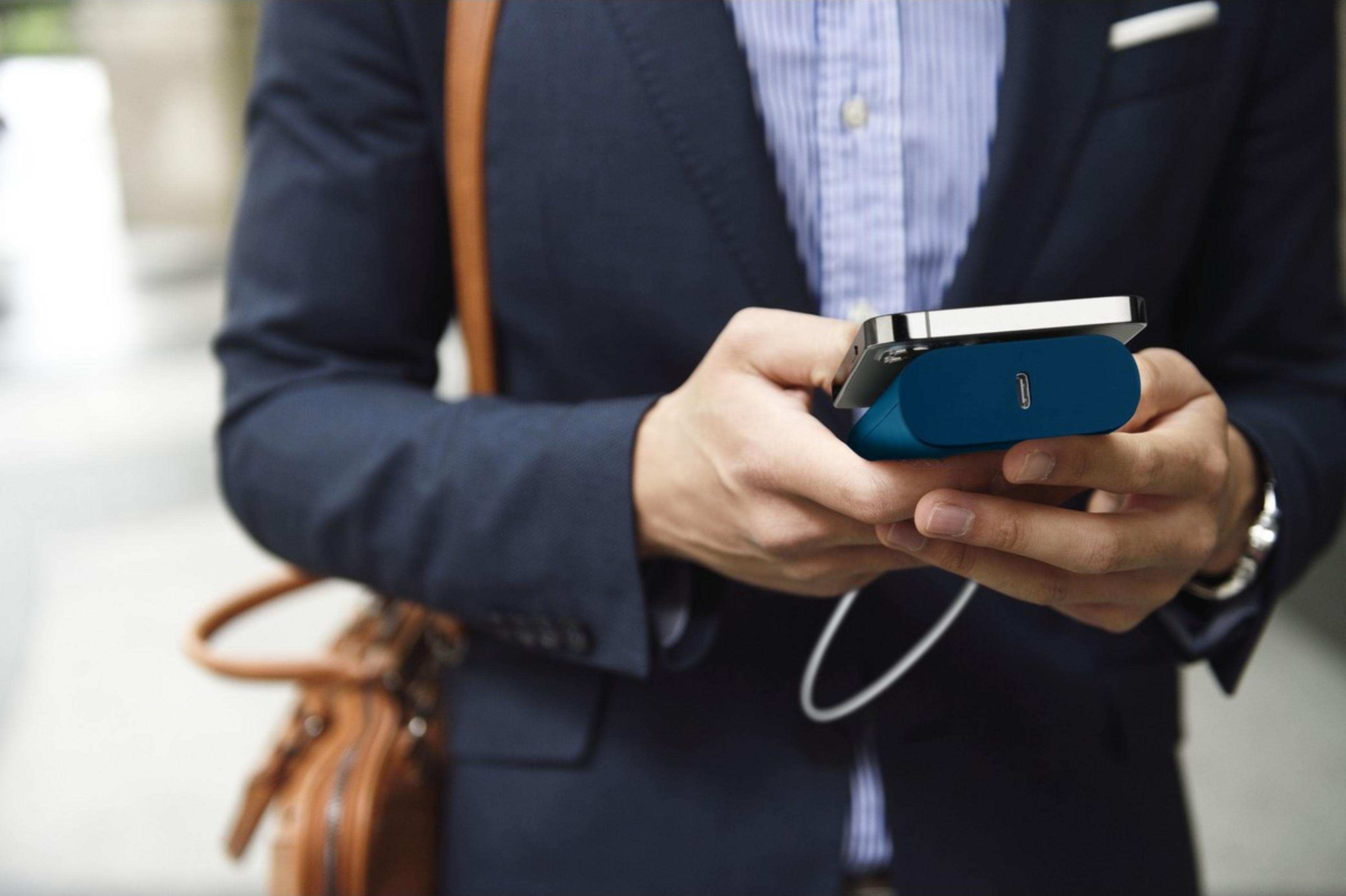 Mann im Anzug mit blauem Ladegerät und Handy in der Hand.