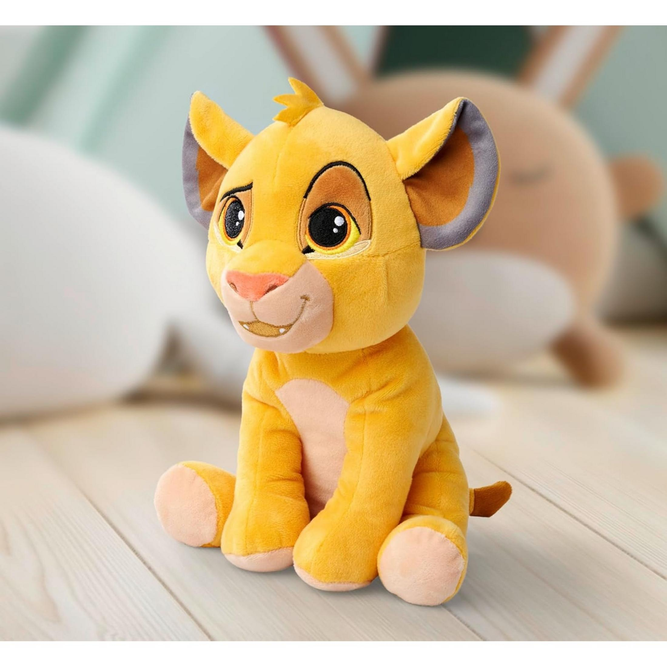 Peluche di Simba seduto su pavimento in legno, sfondo sfocato.