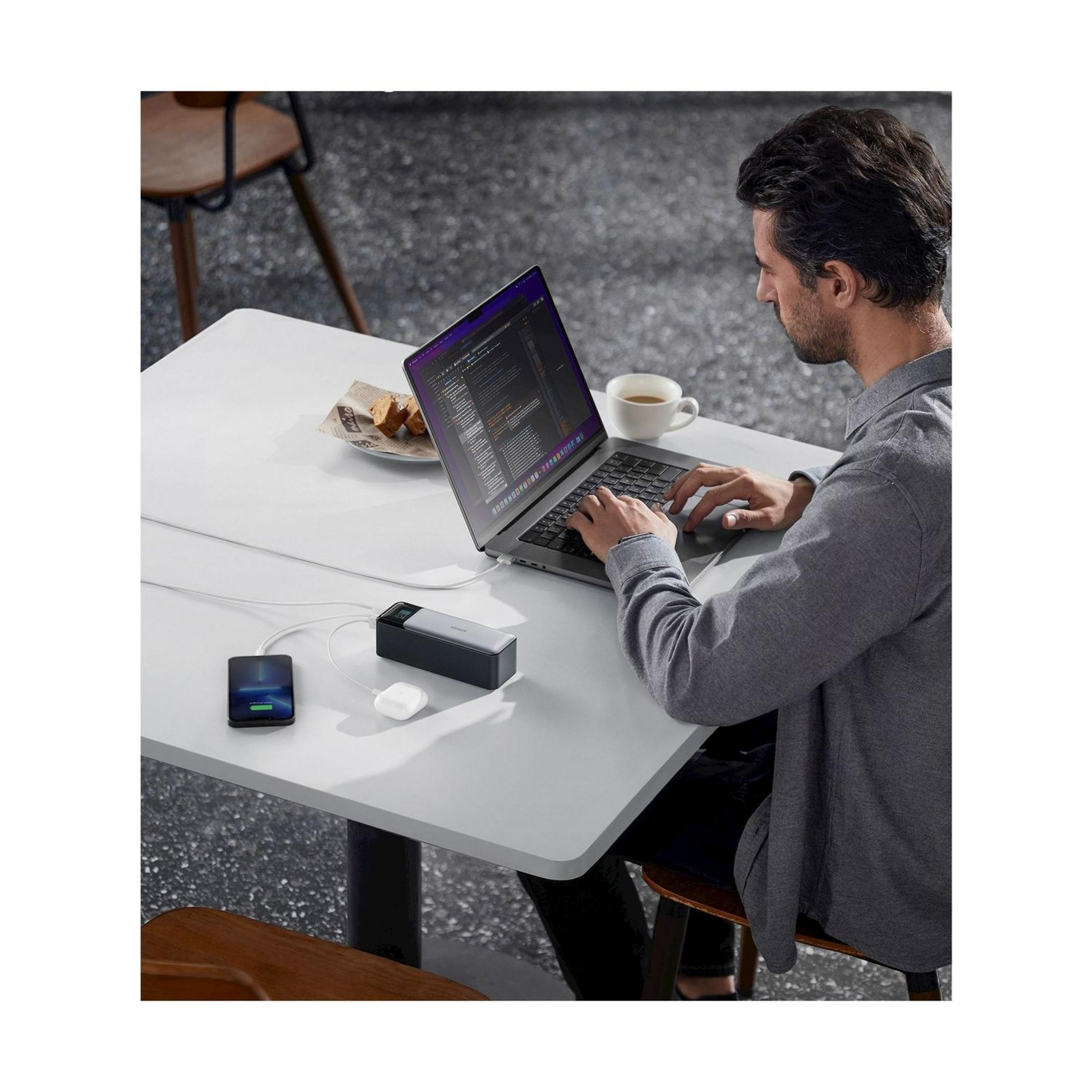 Mężczyzna pracuje na laptopie z telefonem, ładowarką i słuchawkami.