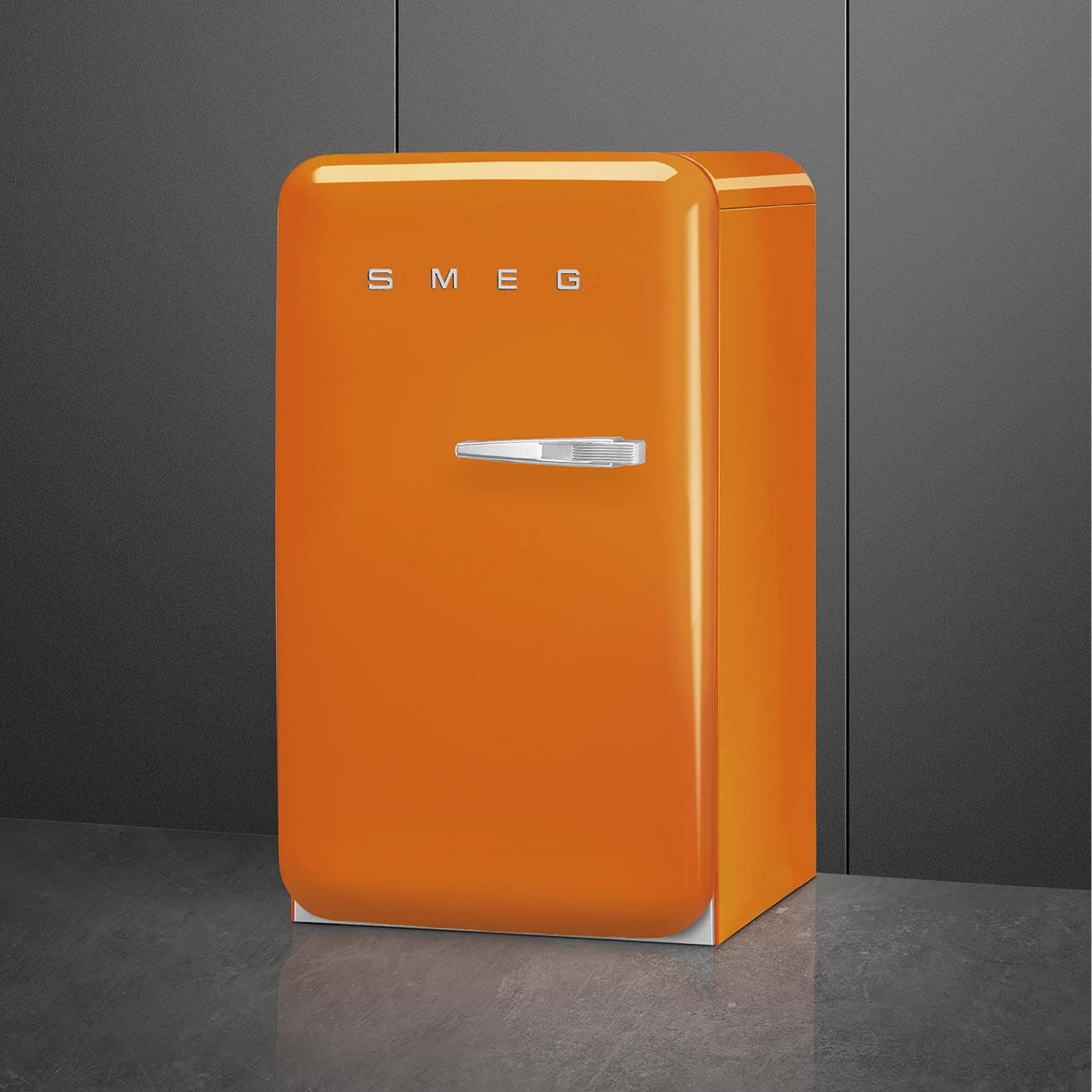 Un refrigerador naranja brillante con asa plateada sobre suelo oscuro.
