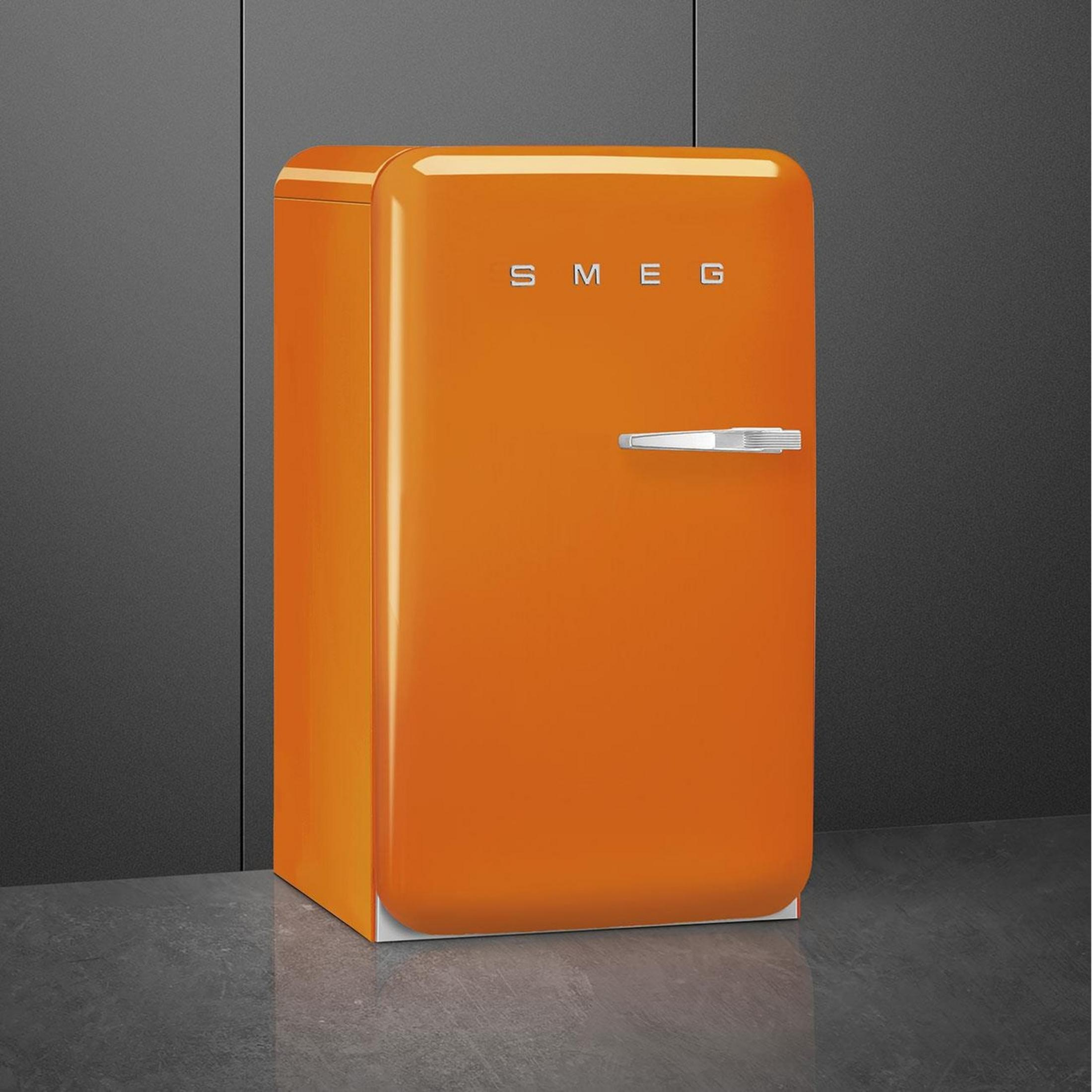 Un refrigerador Smeg naranja con asa plateada sobre suelo gris.