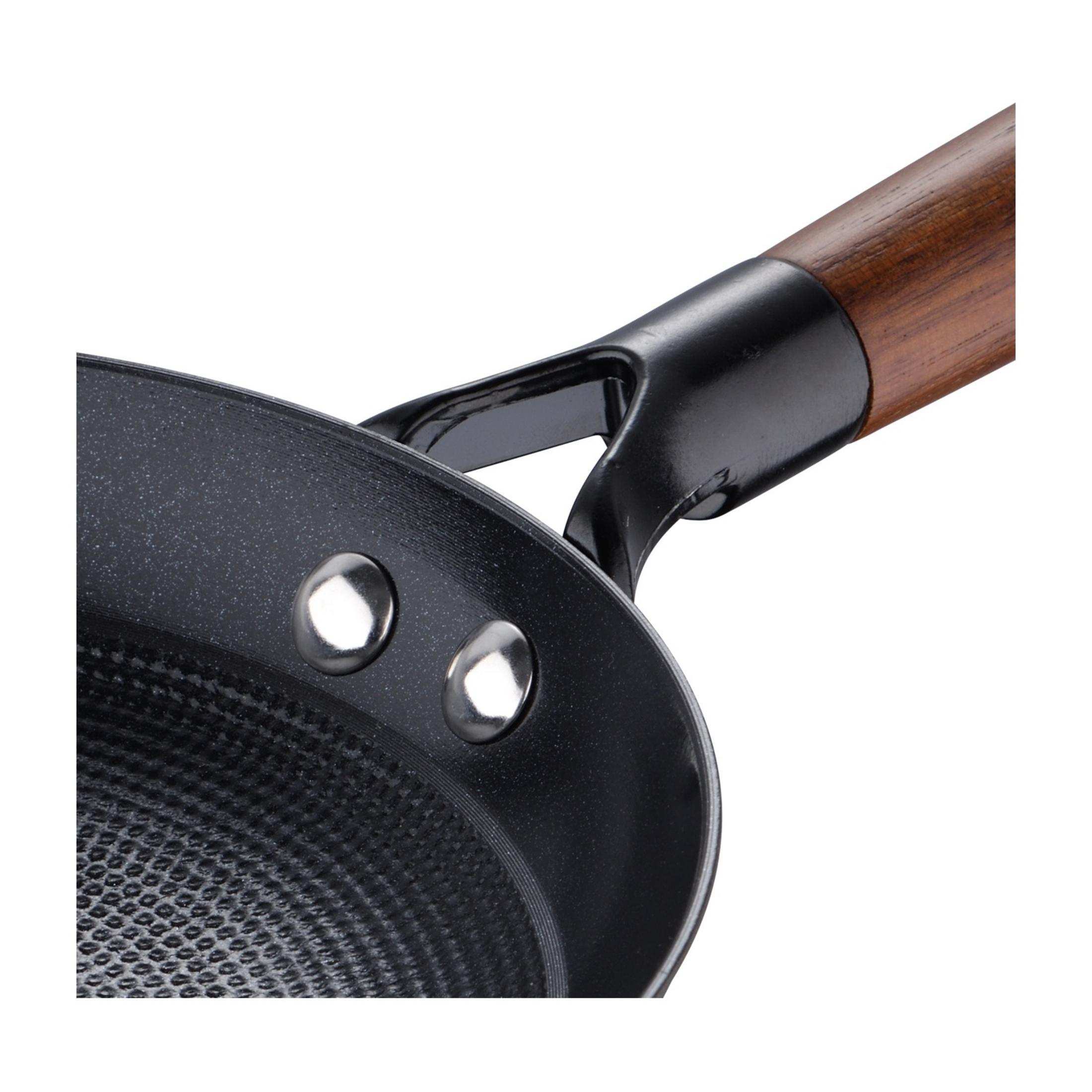 Primo piano di una padella nera con manico in legno e rivetti.