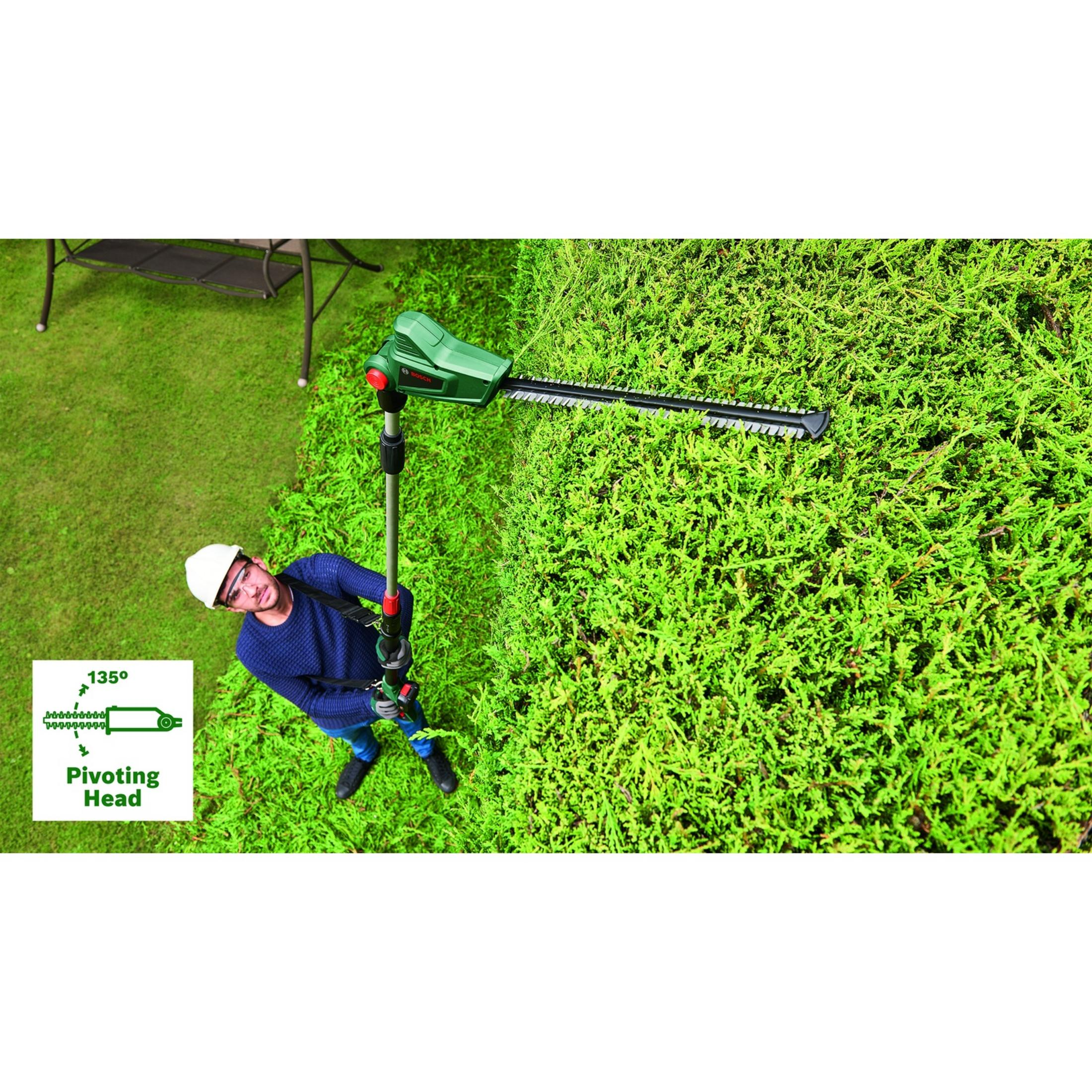 Mężczyzna przycina żywopłot nożycami na wysięgniku. Trawa i meble ogrodowe.