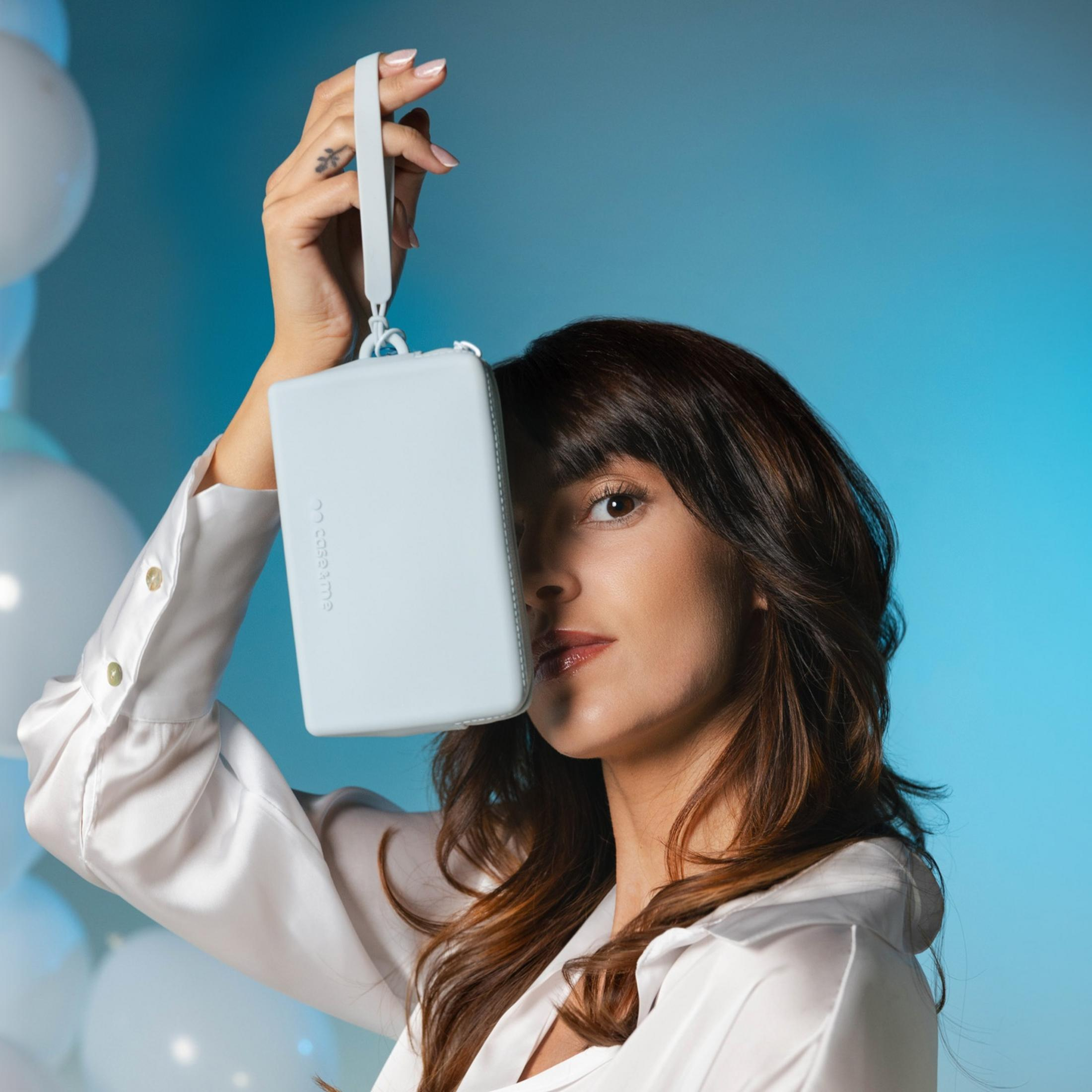 Una donna con i capelli castani tiene una borsa azzurra davanti al viso.