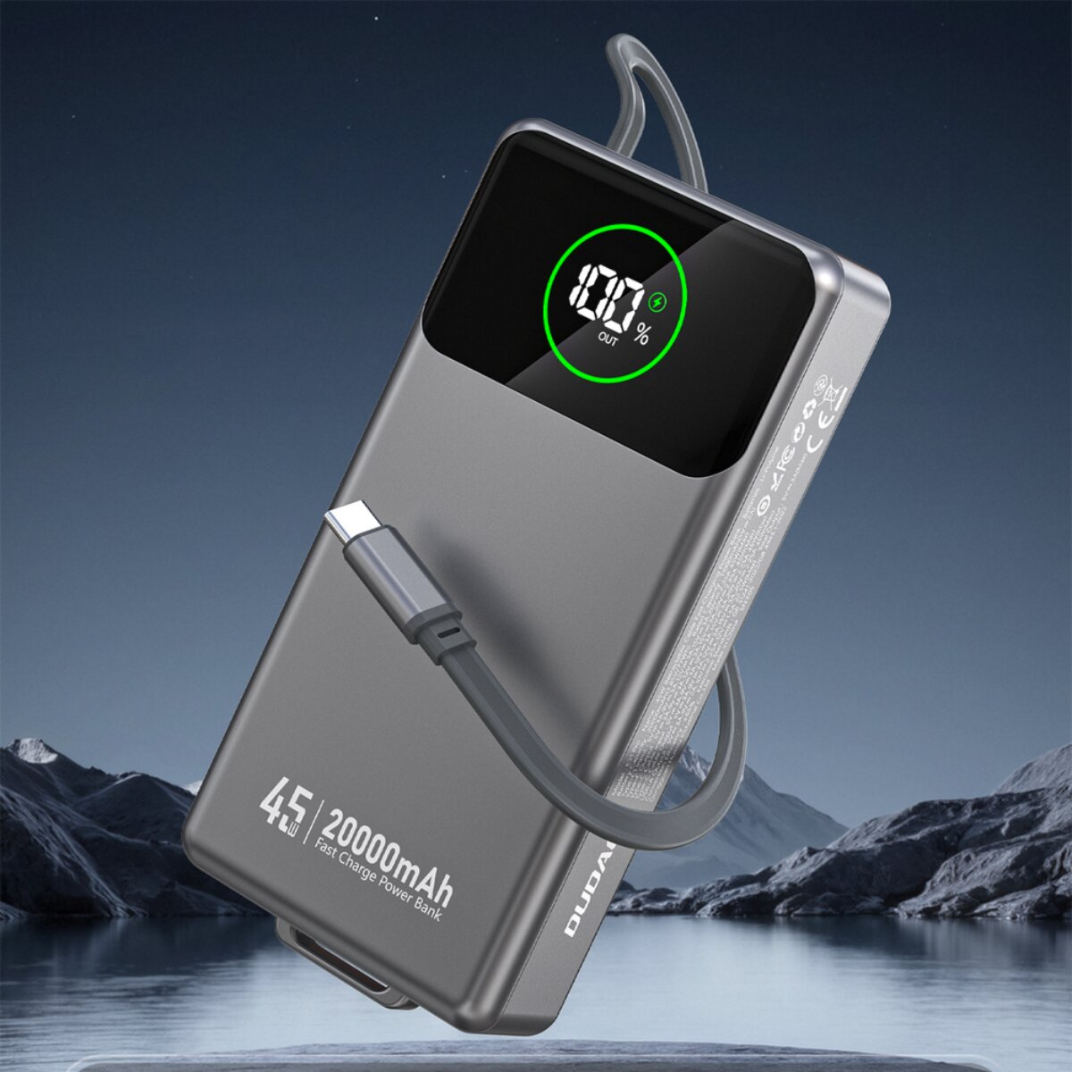 Grauer Powerbank mit 100% Ladung und USB-C-Kabel, vor Berg- und Wasserlandschaft.
