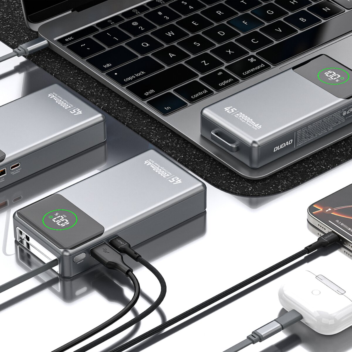 Graue Powerbanks und ein Laptop mit angeschlossenen Ladekabeln und Kopfhörern.