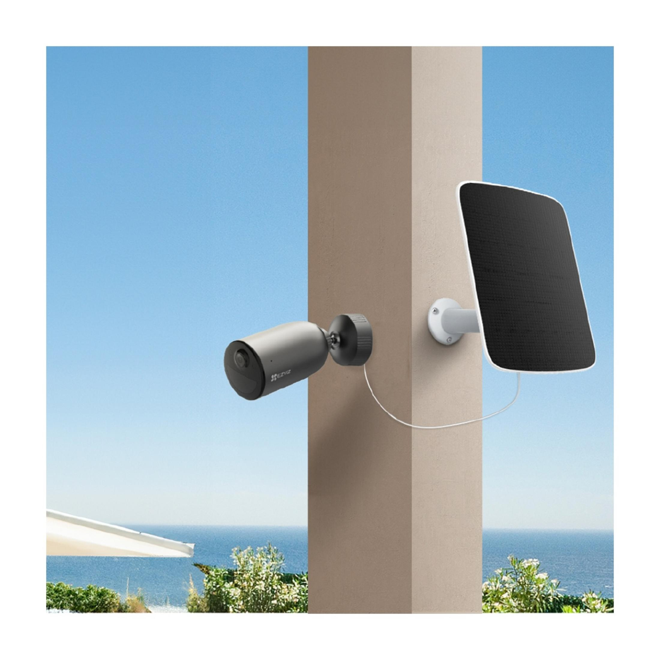 Szara kamera bezpieczeństwa i panel słoneczny zamontowane na ścianie, z morzem w tle.