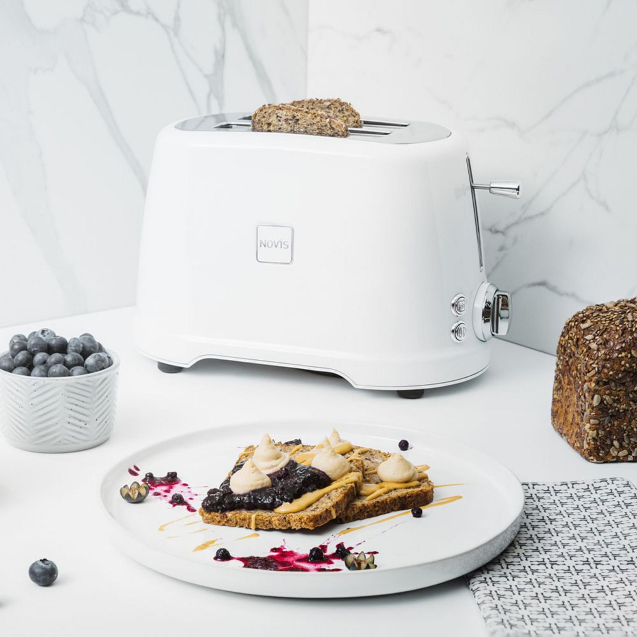 Un grille-pain blanc avec toasts, baies et pain sur un comptoir en marbre.