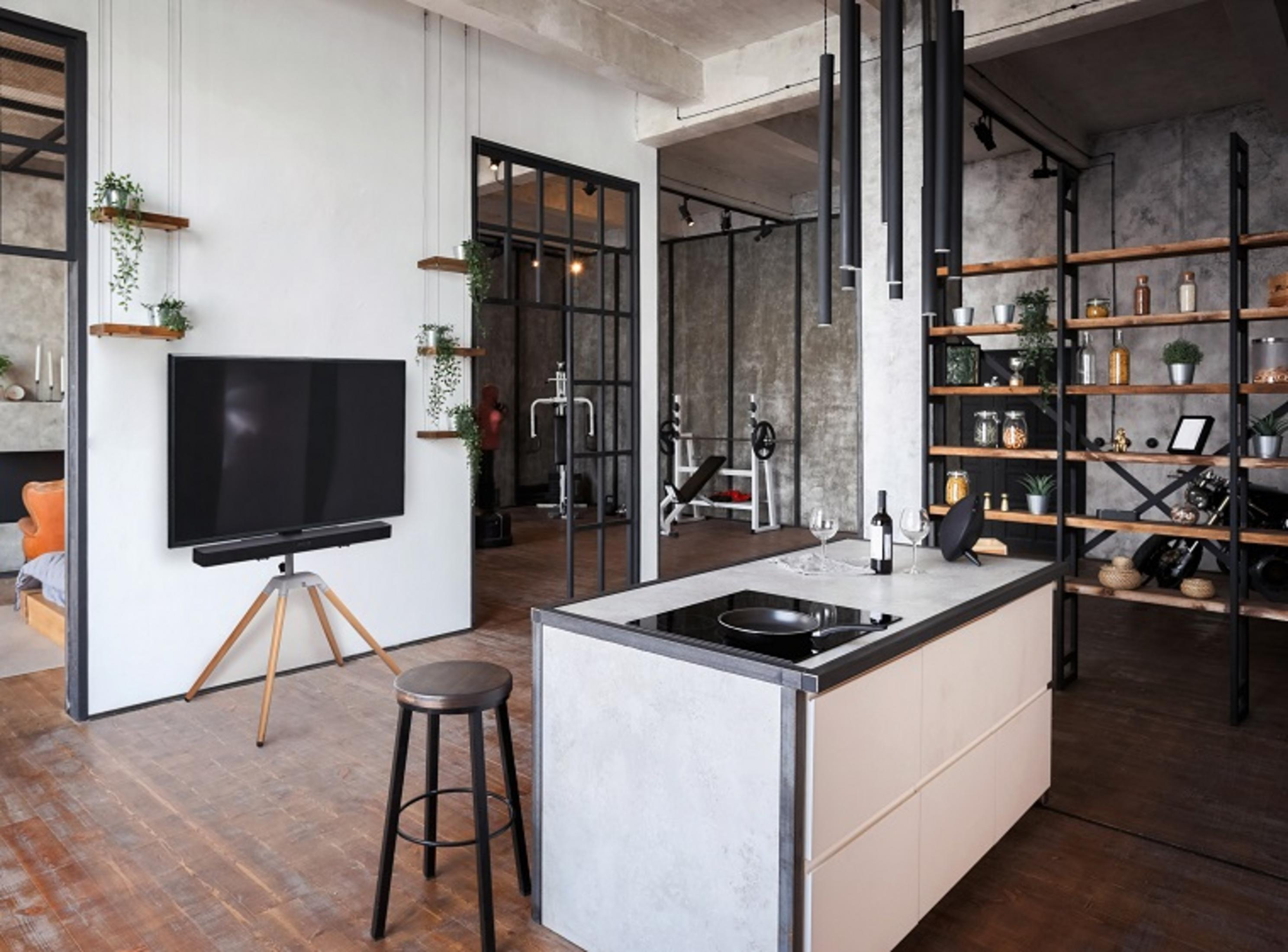 Loft mit Küche, Fitnessbereich und Wohnzimmer. Dunkle Holzböden, Betonwände.