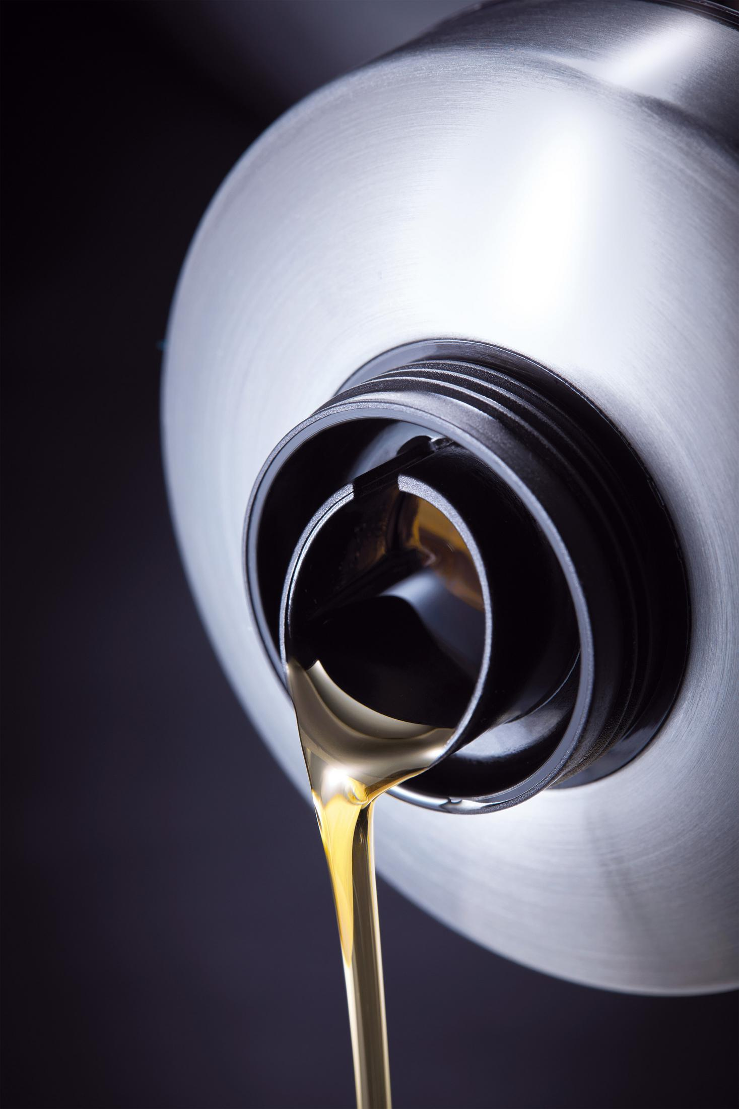 Goldene Flüssigkeit fließt aus einem silbernen Behälter mit schwarzem Deckel.