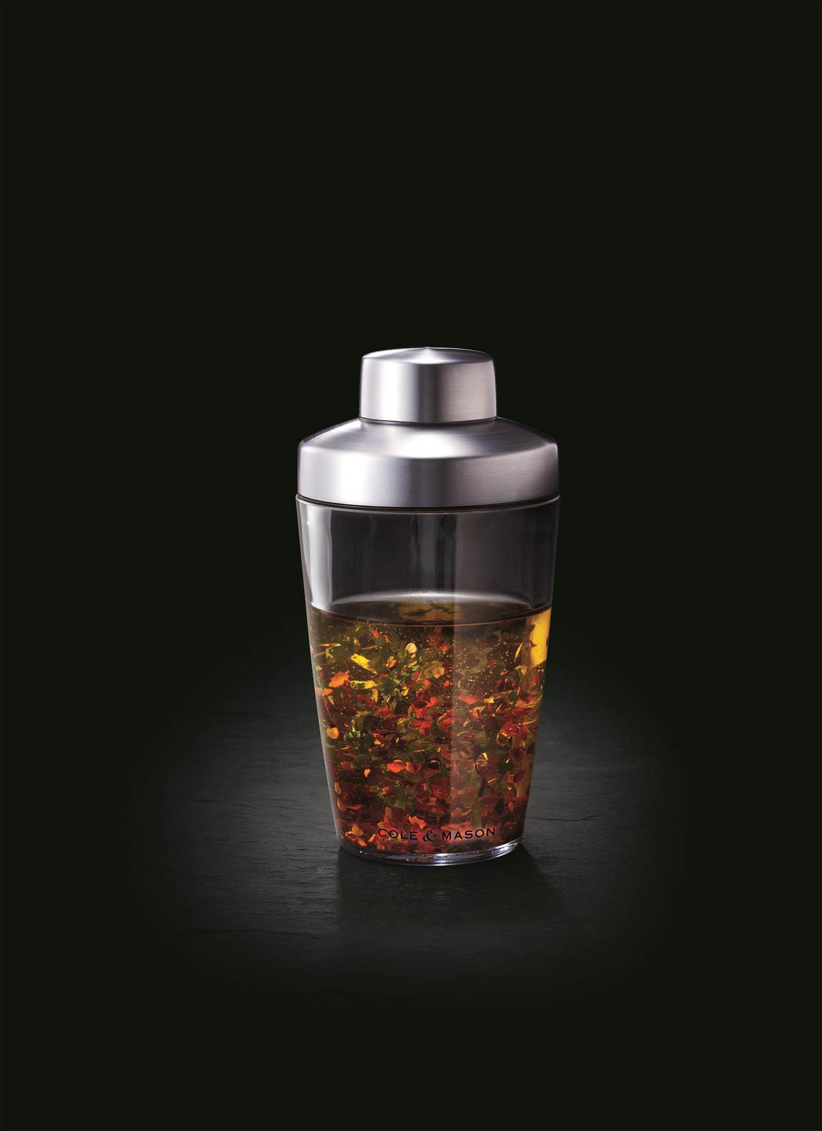 Ein Salatdressing-Shaker aus Glas und Metall mit Kräutern und Gewürzen.