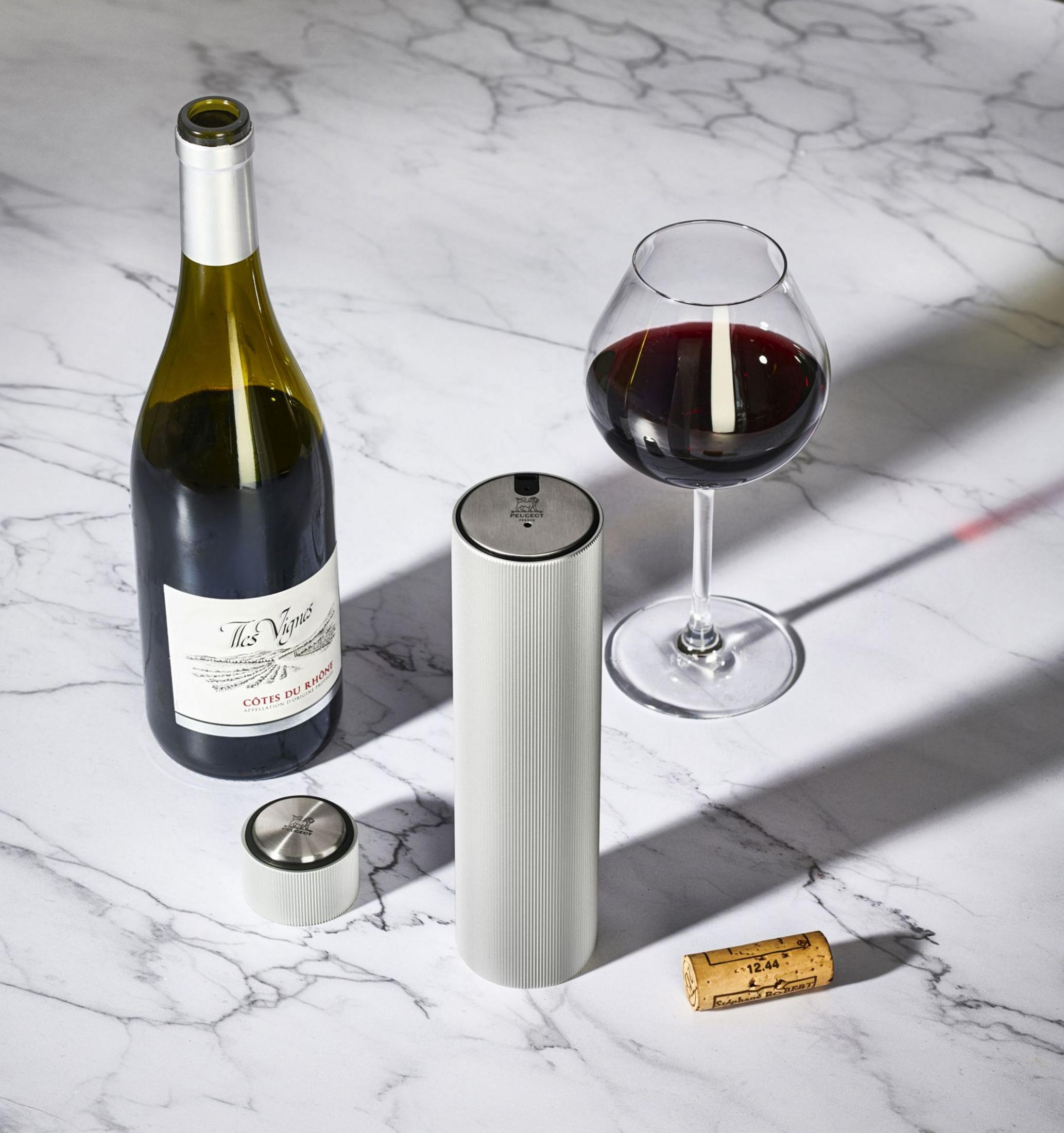 Eine Weinflasche, ein Korkenzieher, ein Glas Rotwein und ein Korken auf Marmor.