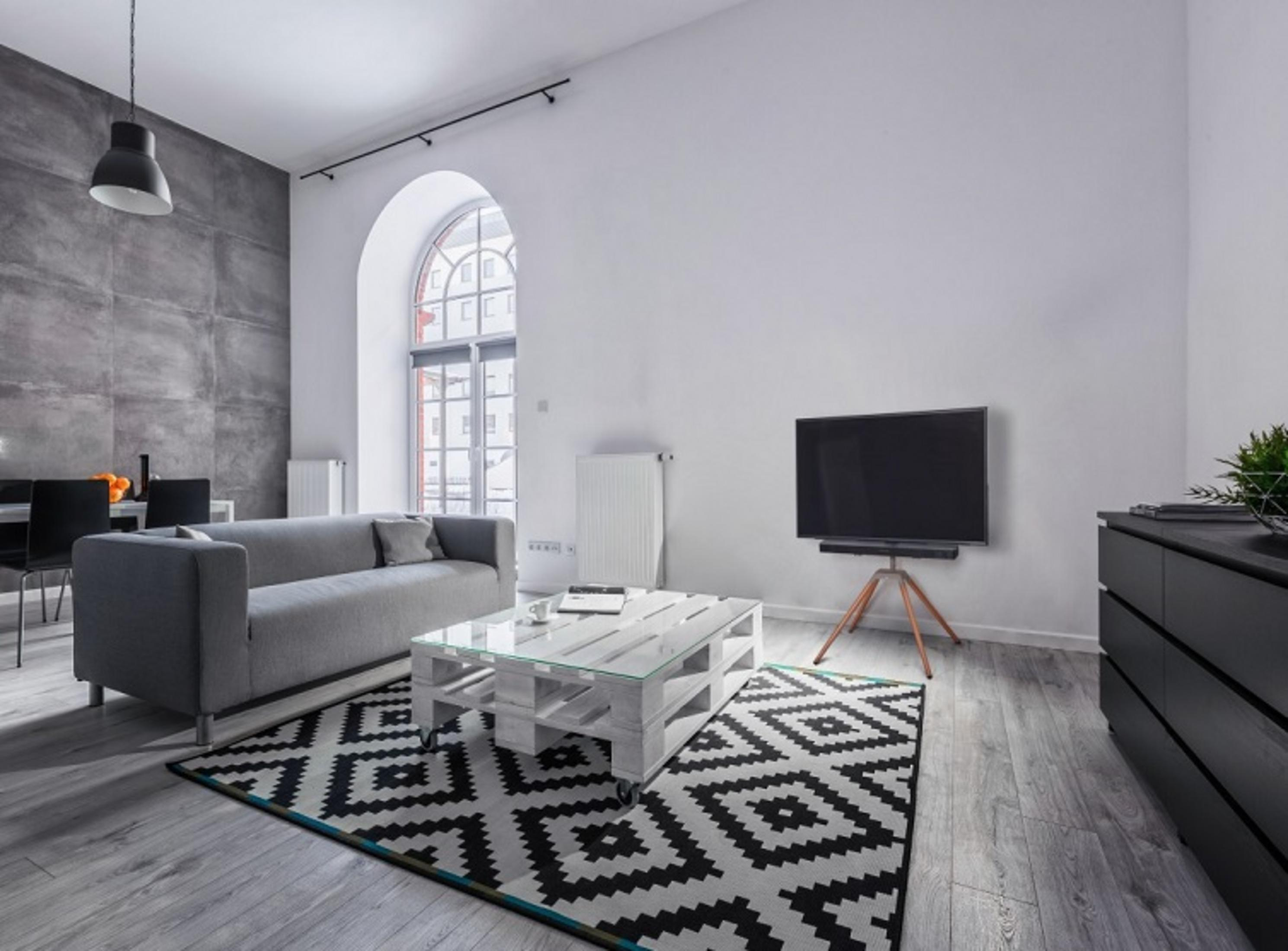 Graues Sofa, weißer Paletten-Couchtisch, Teppich, Fernseher und schwarze Kommode.