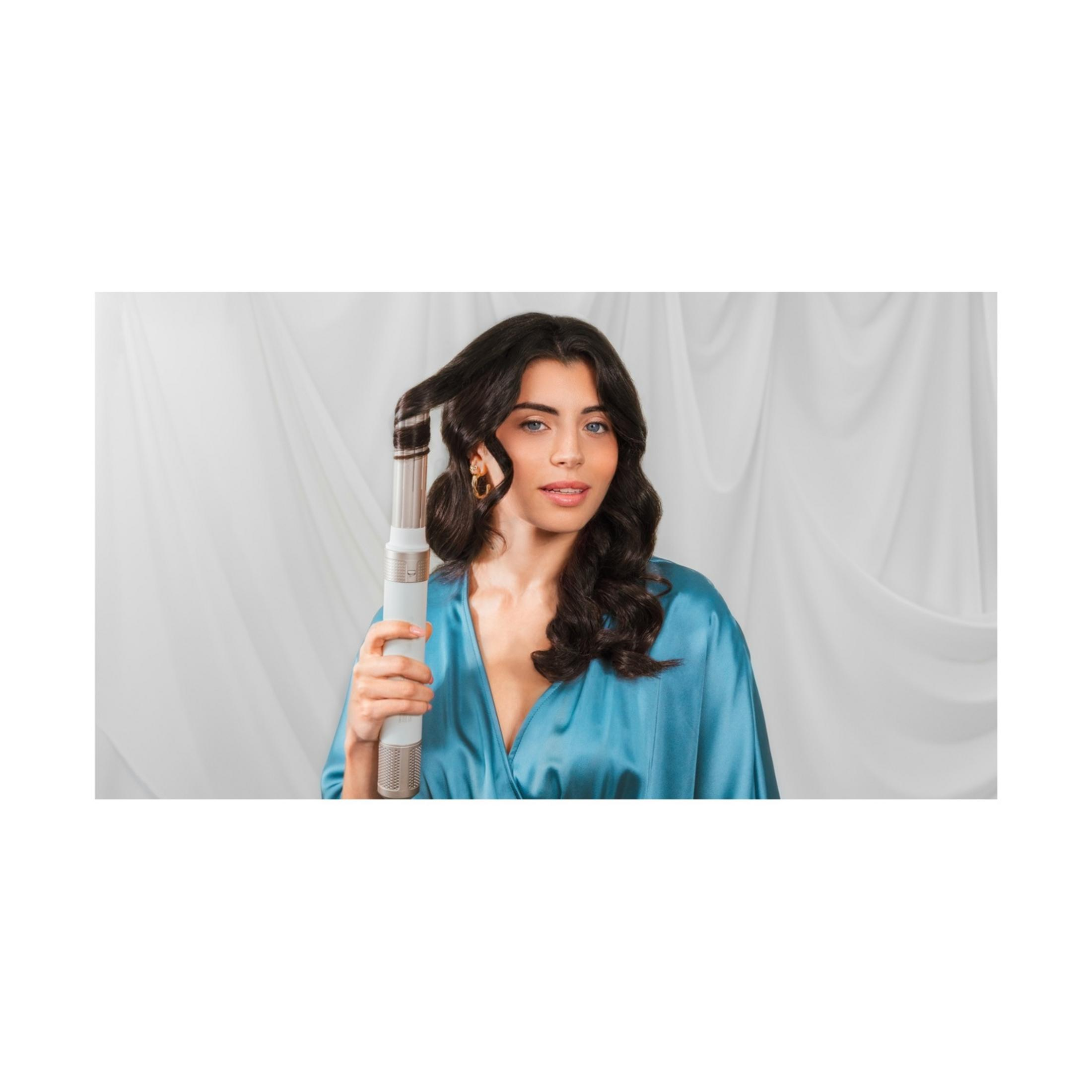 A woman with dark hair in a blue silk dress holds a hair dryer.