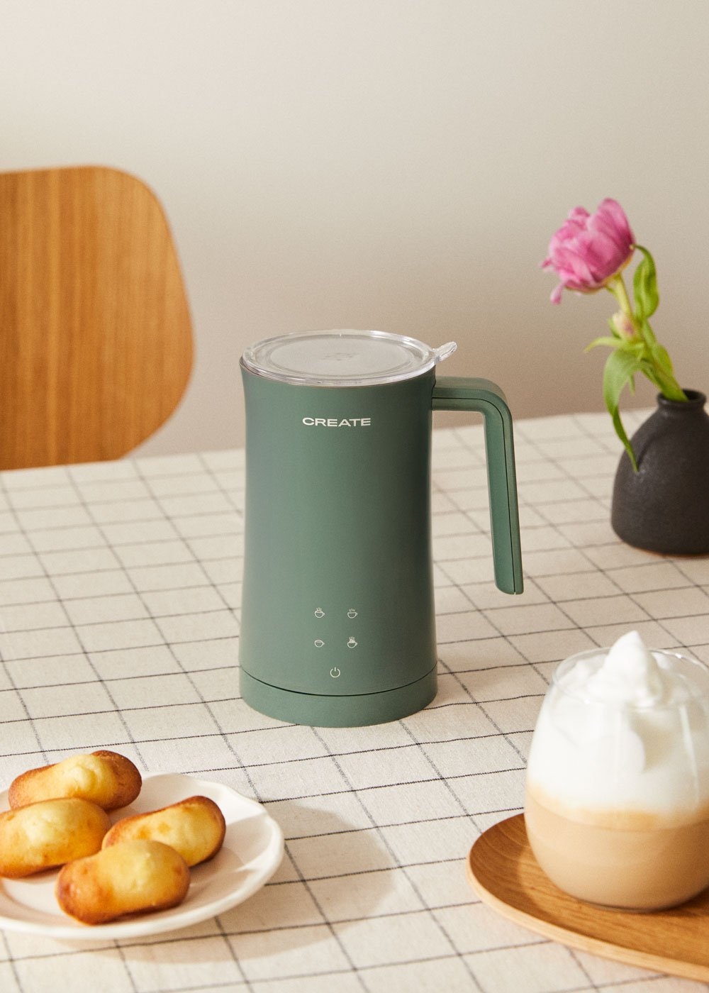 Un espumador de leche verde sobre una mesa a cuadros con galletas y un café.