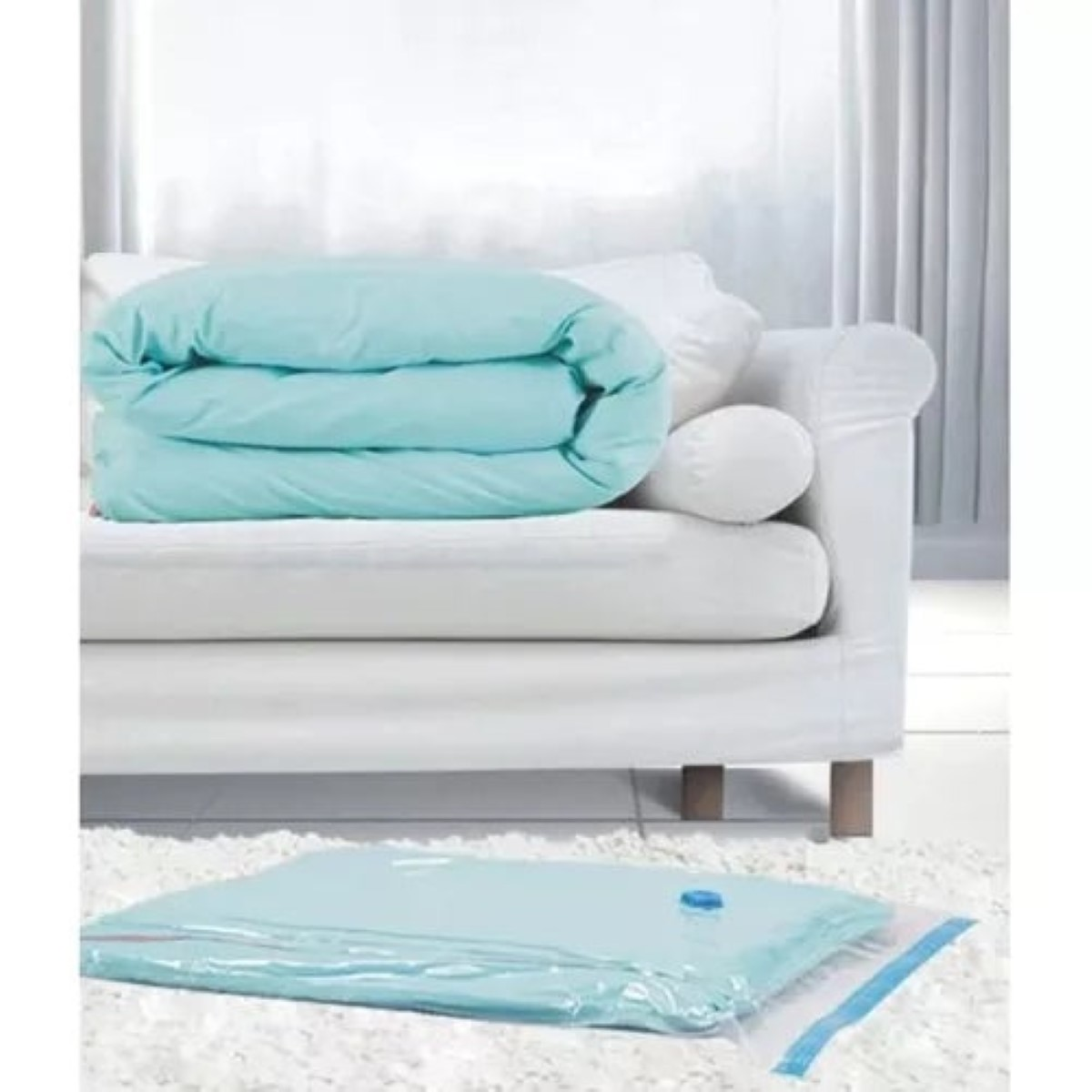 Un edredón azul claro plegado descansa sobre un sofá blanco. A su lado hay una bolsa de vacío.