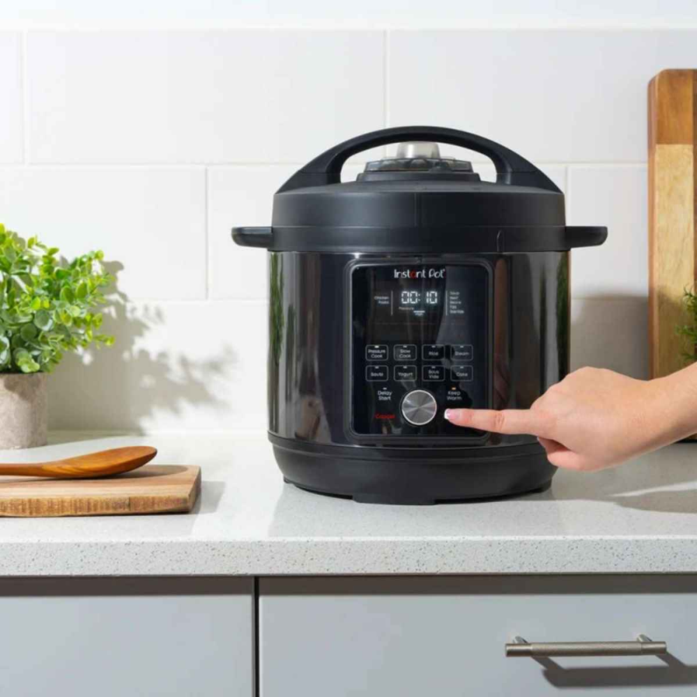 A hand presses a button on a black Instant Pot on a kitchen counter.
