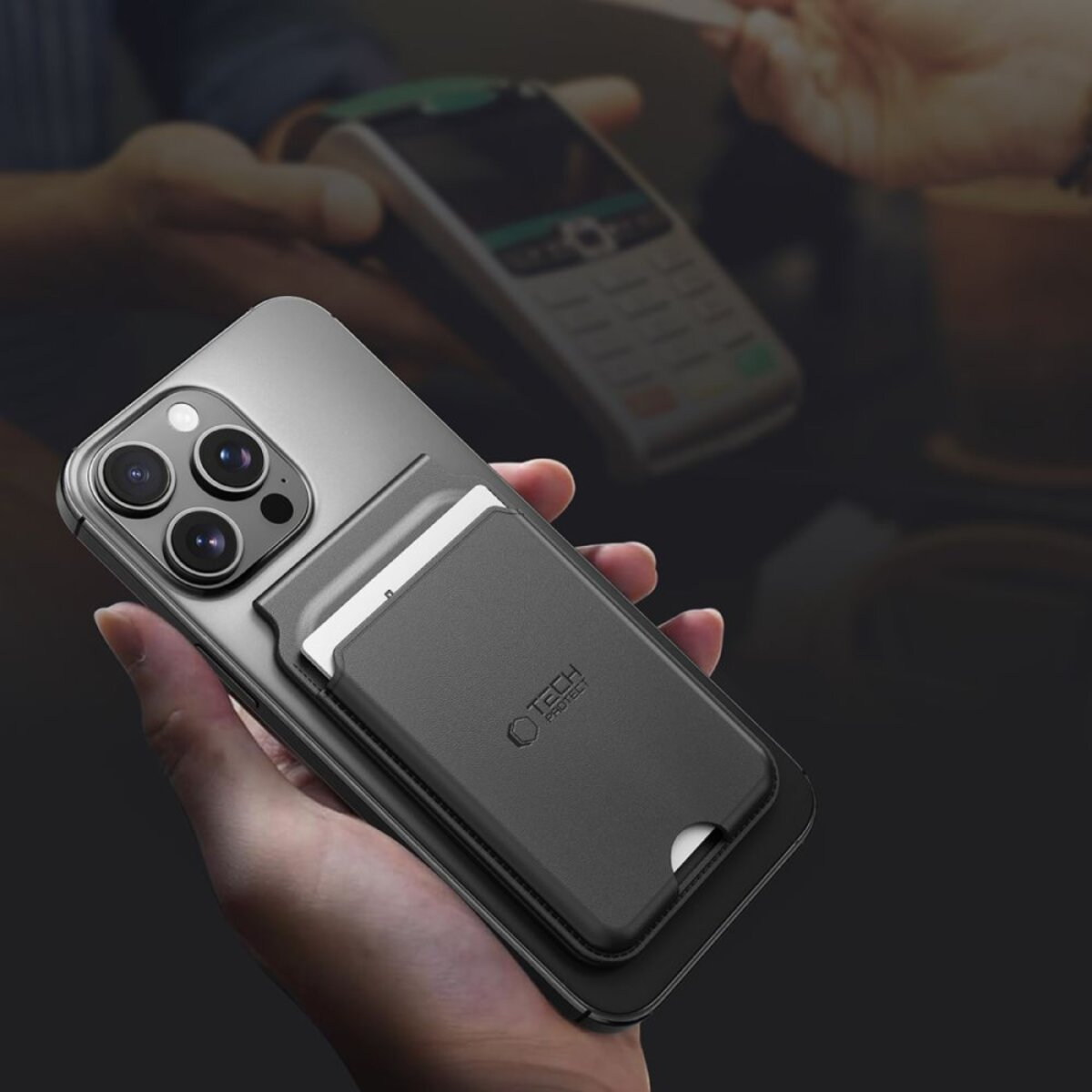 Hand hält Smartphone mit Kartenhalter; im Hintergrund ein Terminal.