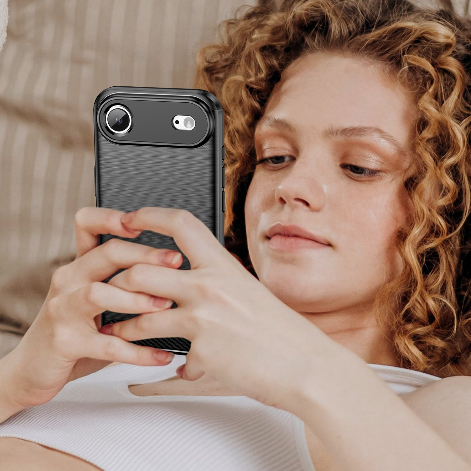 Una mujer con pelo rizado está acostada usando un smartphone negro.
