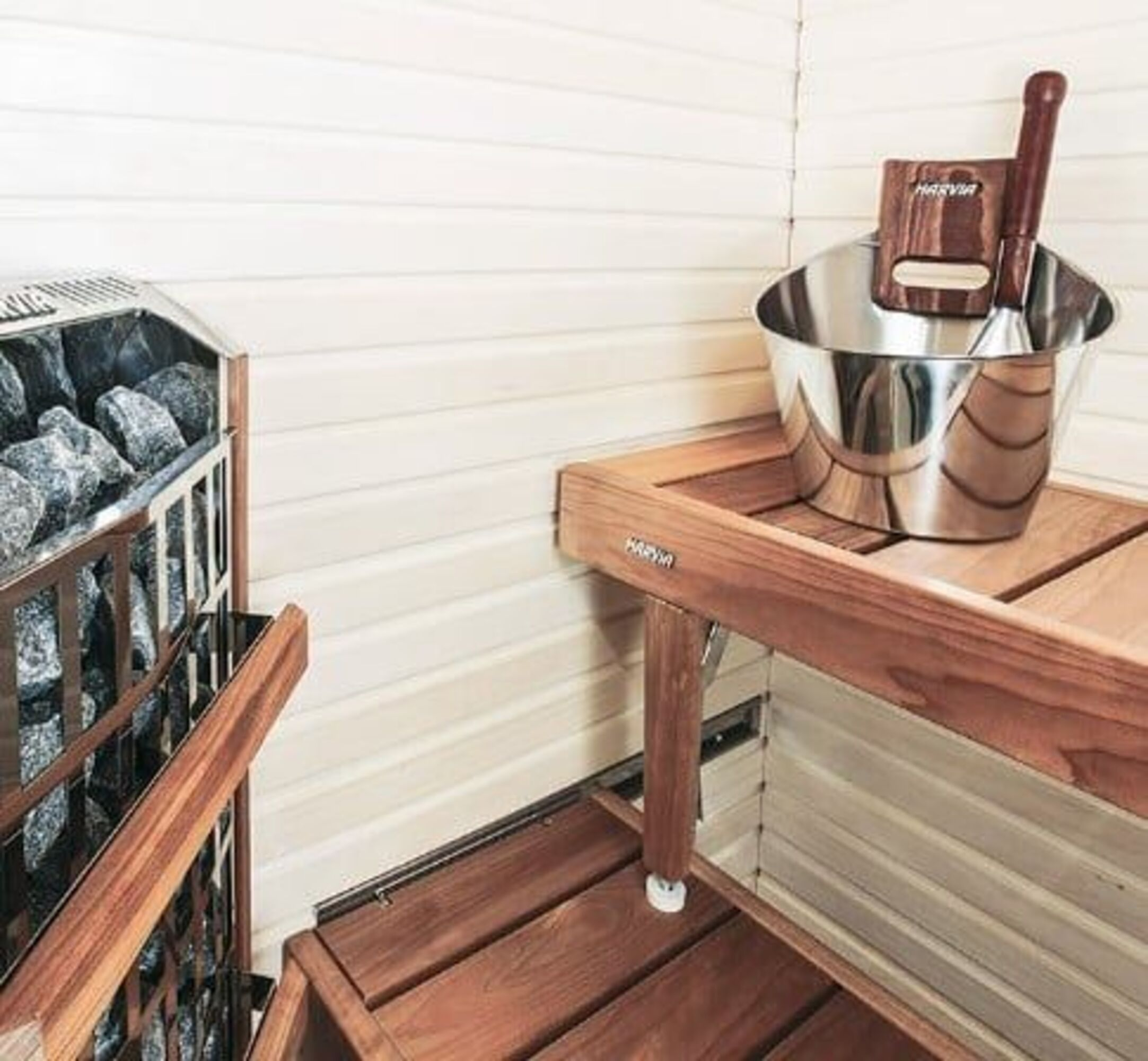 Horno de sauna con piedras, cubo de madera con cucharón en banco de madera.