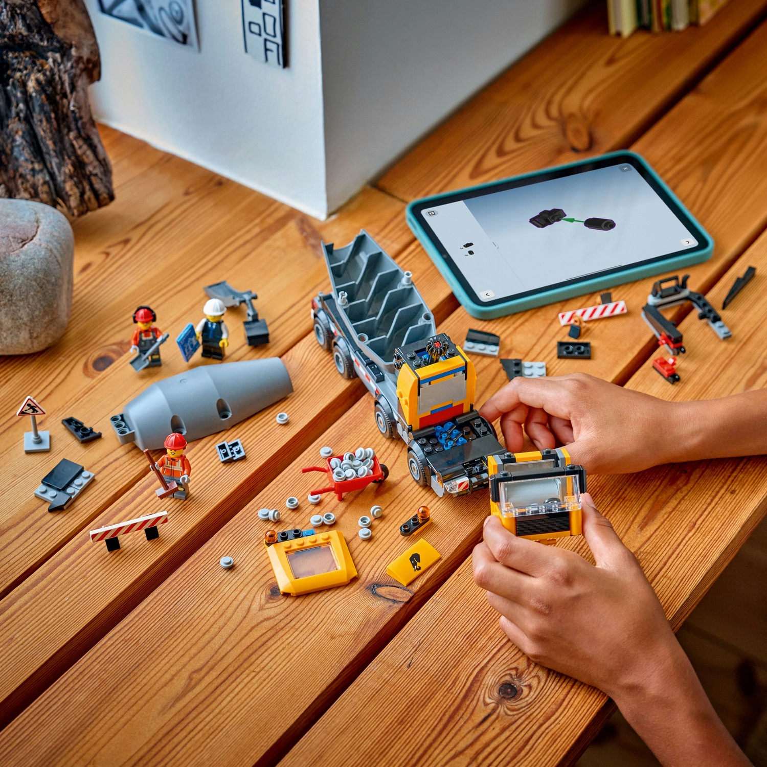 Ręce budują ciężarówkę budowlaną Lego z instrukcjami na tablecie. Figurki, betoniarka, taczka.