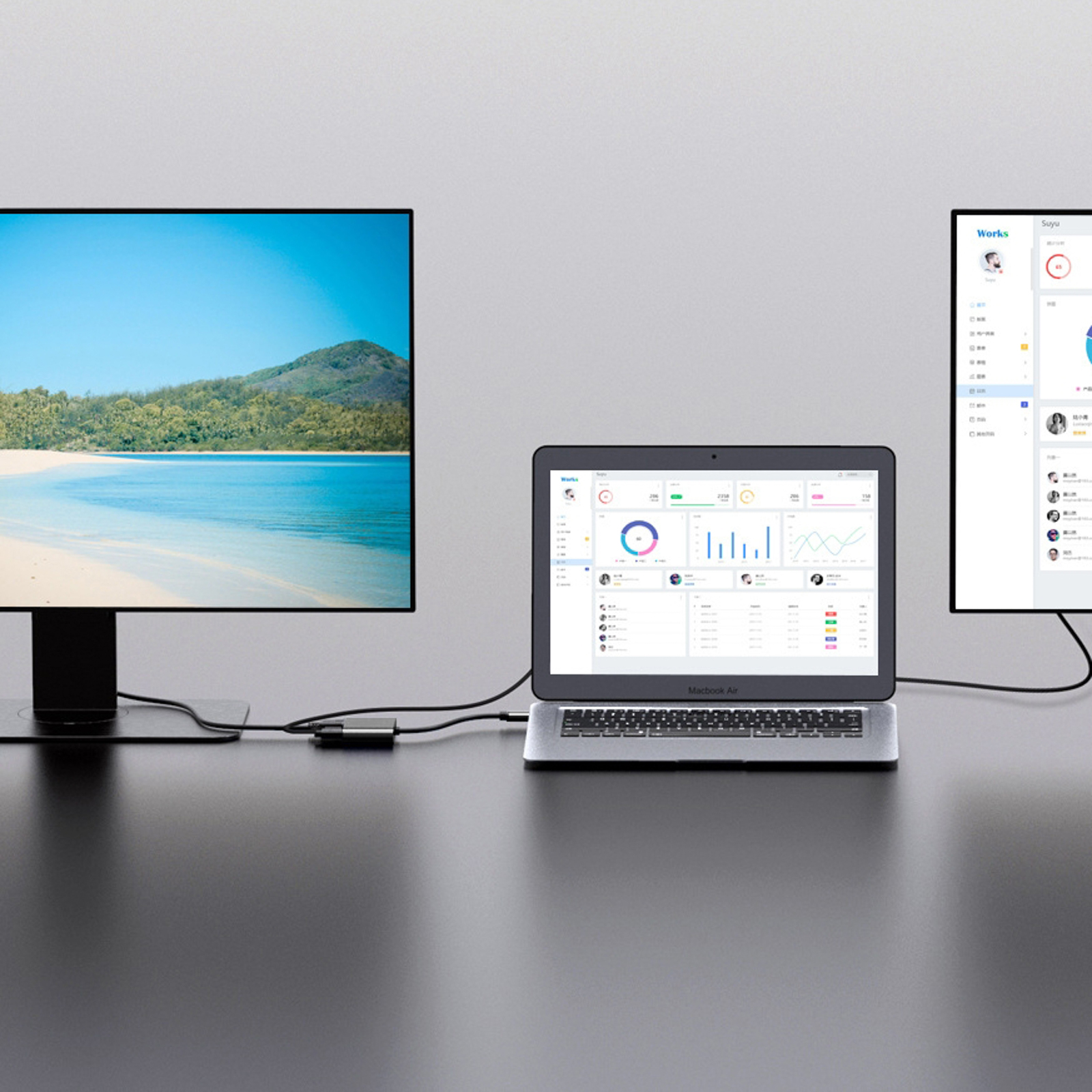Un laptop e due monitor su una scrivania. Un monitor mostra una scena di spiaggia, il laptop e l'altro monitor mostrano dati.