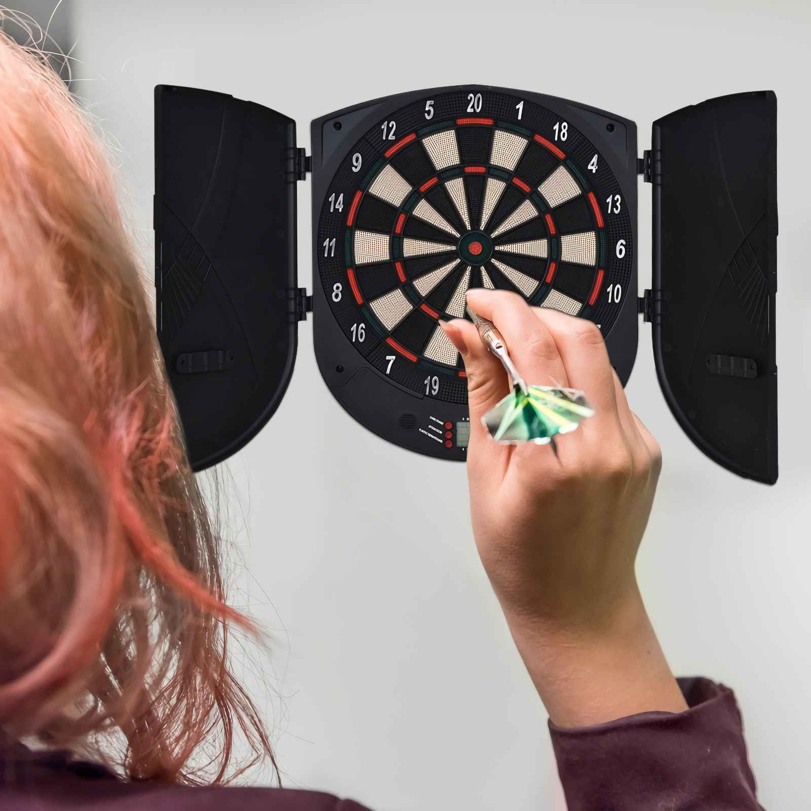Person wirft einen Dartpfeil auf eine beleuchtete Dartscheibe mit Zahlen.