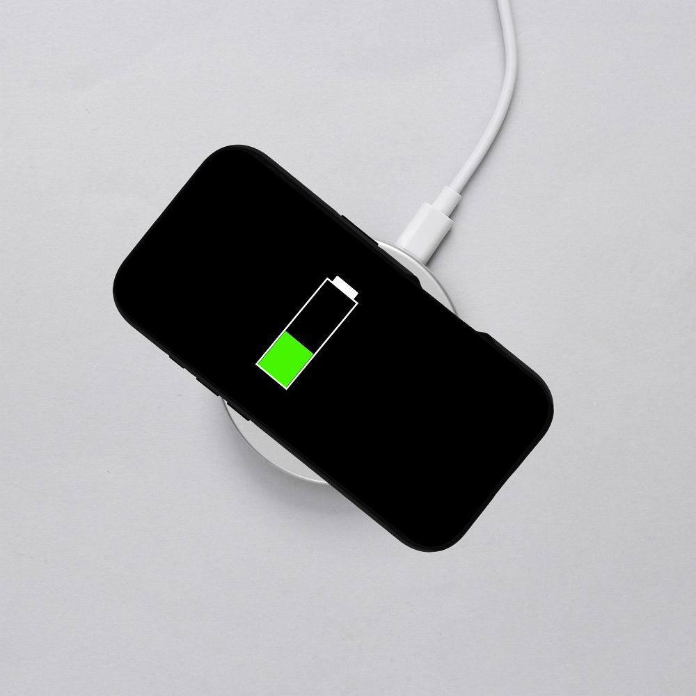 Ein schwarzes Smartphone wird kabellos auf einem weißen Pad geladen. Das Akkusymbol ist halb voll.